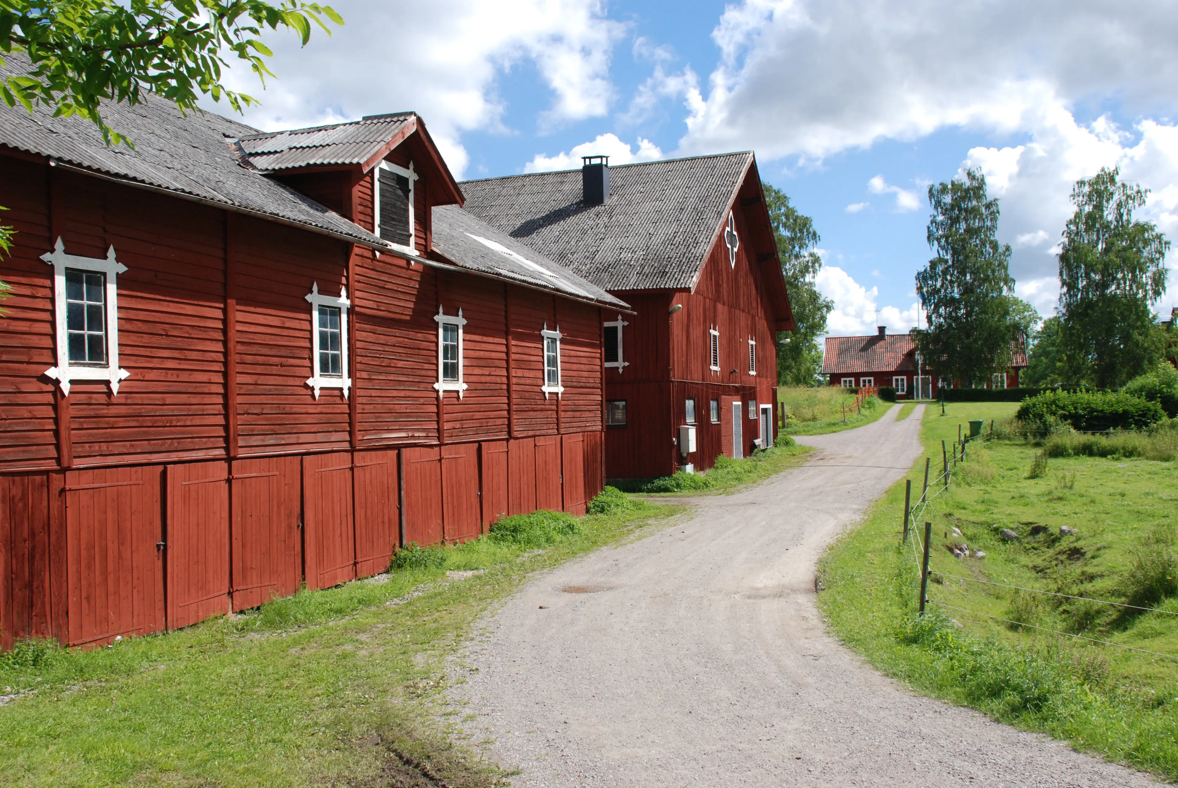 Ekonomibyggnader, Kungsbergs kungsgård. Stora, rödmålade träbyggnader. Sommar och grönska.