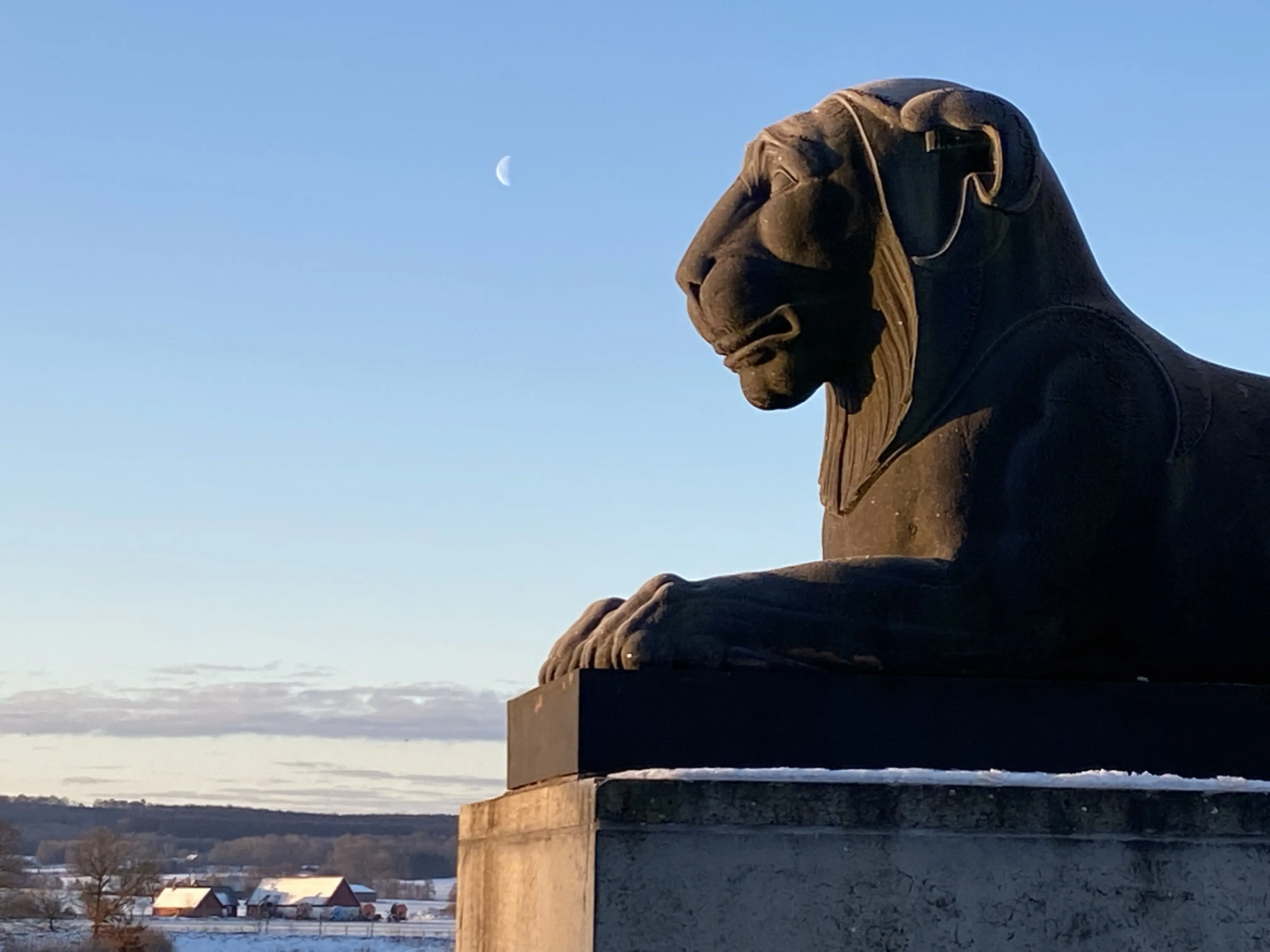 Kvidingemonumentet. Närbild på ett av sockelns stenlejon. På himlen syns halvmånen. Vinter och snö.