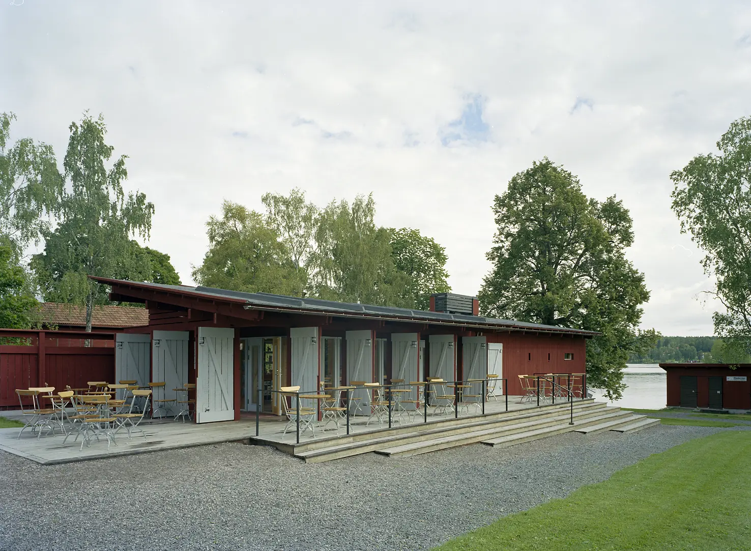 Modern servicebyggnad i falurött trä. Vy mot vattnet. Sommar och grönska.