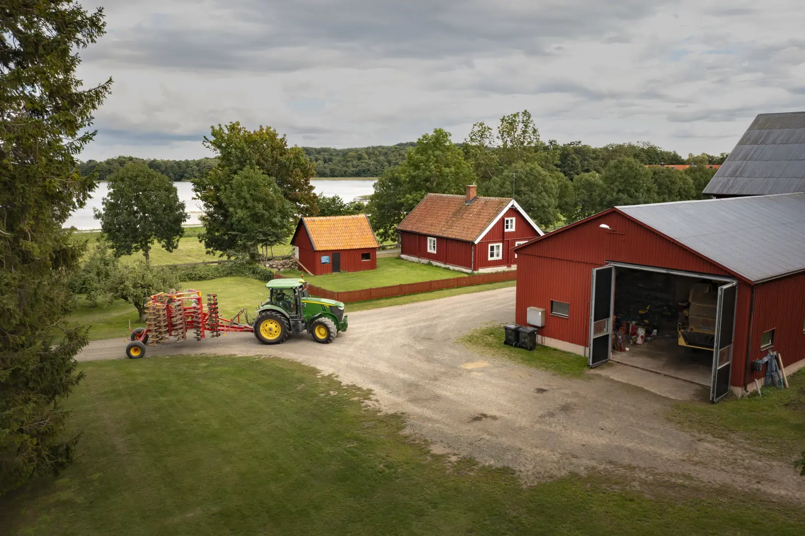 Röda träbyggnader och en grön traktor med en sjö i bakgrunden.