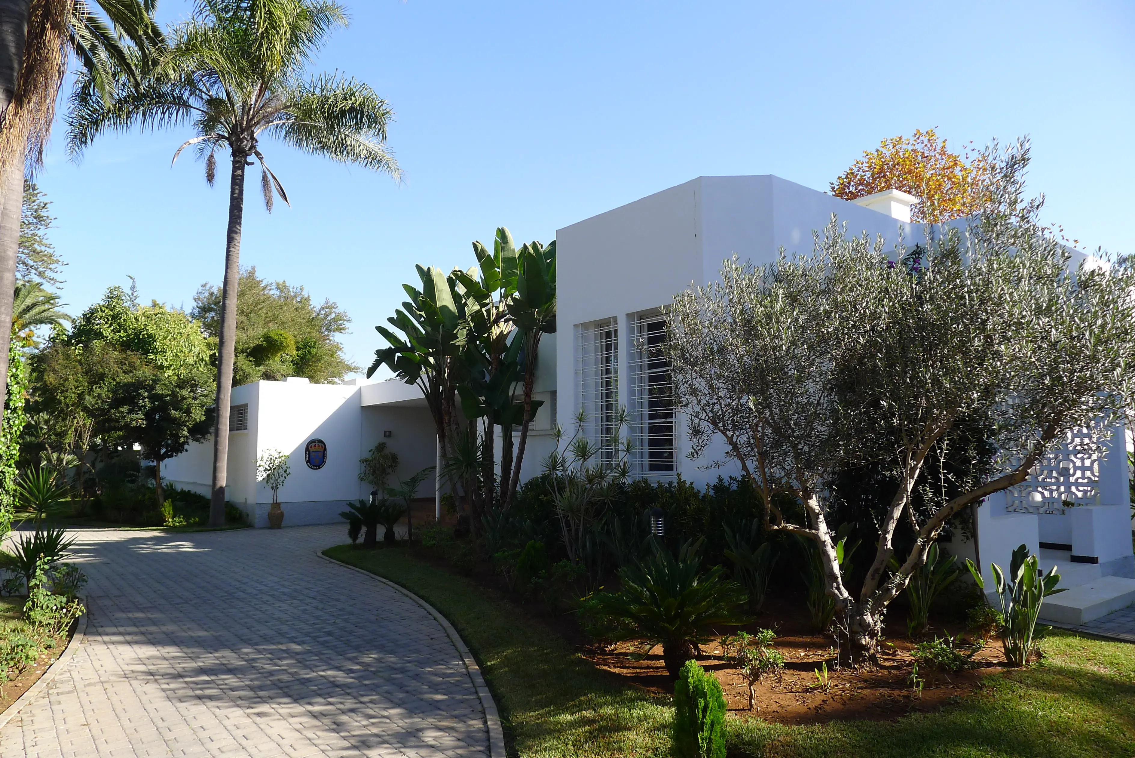 Ambassaden i Rabat, entréfasaden. En modernistisk, vit byggnad i ett plan, omgiven av palmer och lövträd.