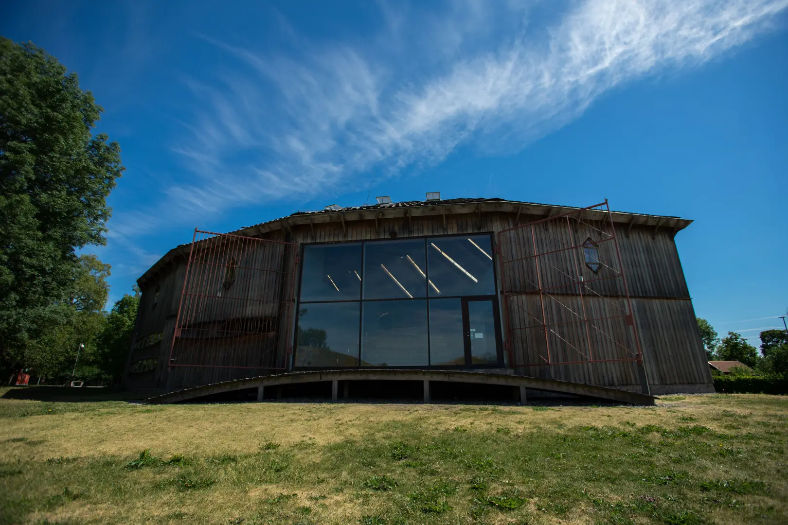 Gamla Uppsala museum. En skeppsformad byggnad klädd med stående träpanel. På långsidan sitter ett stort glasparti.
