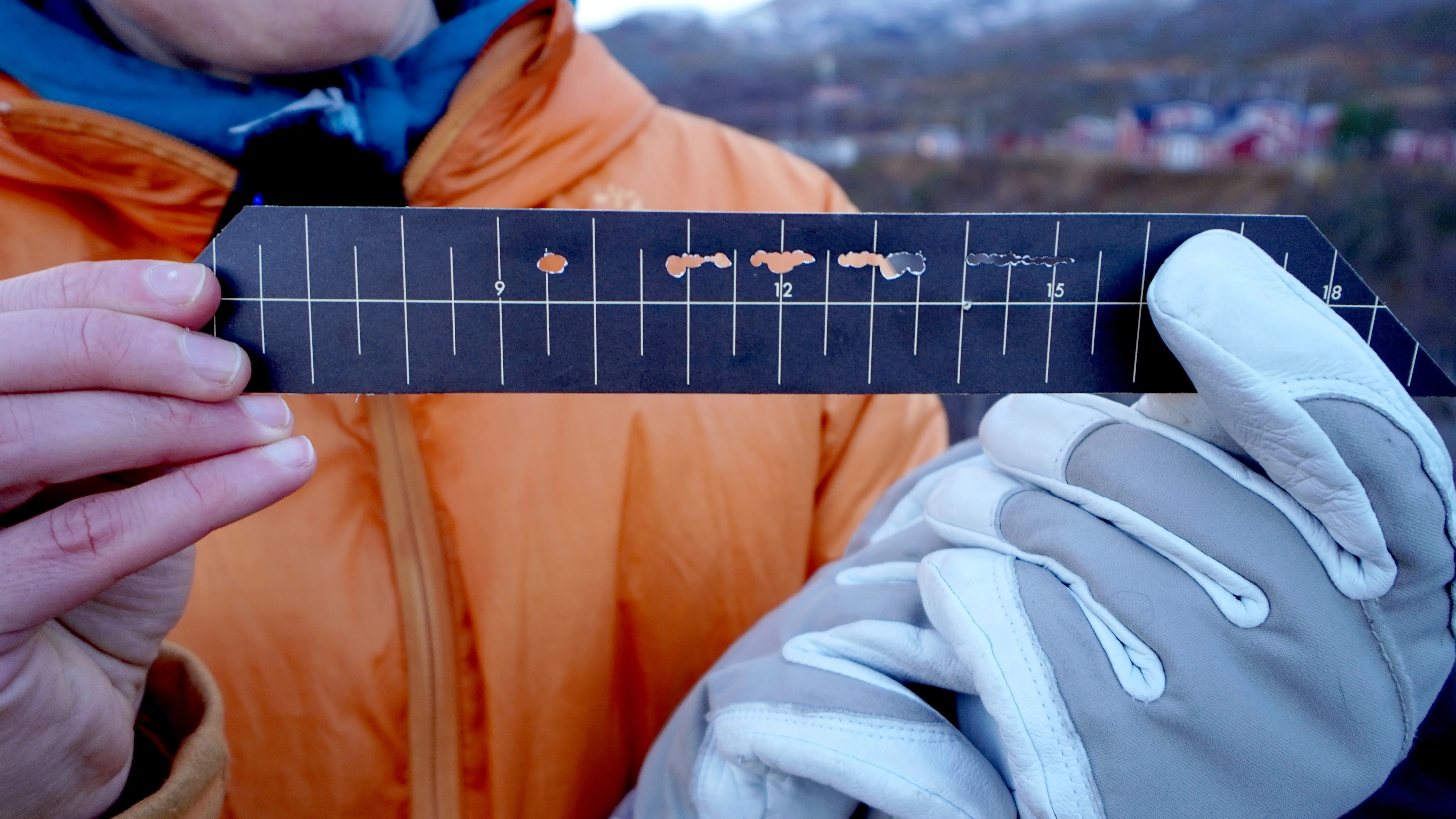 Ett par händer håller i en svart pappersremsa med ljusa, vertikala streck som tidsangivelser. I pappret finns ett antal sönderbrända hål.