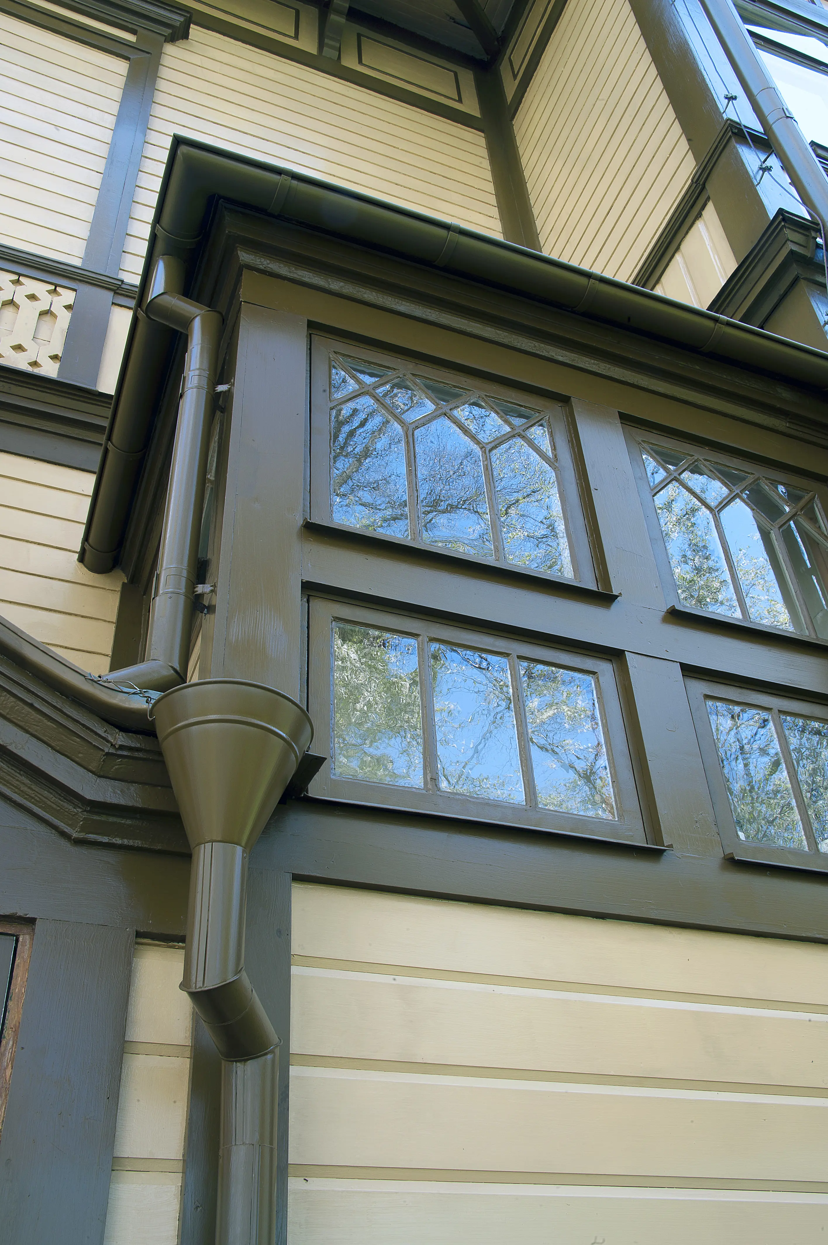 En ljus träfasad med grönmålade fönster och stuprör målade i samma nyans.