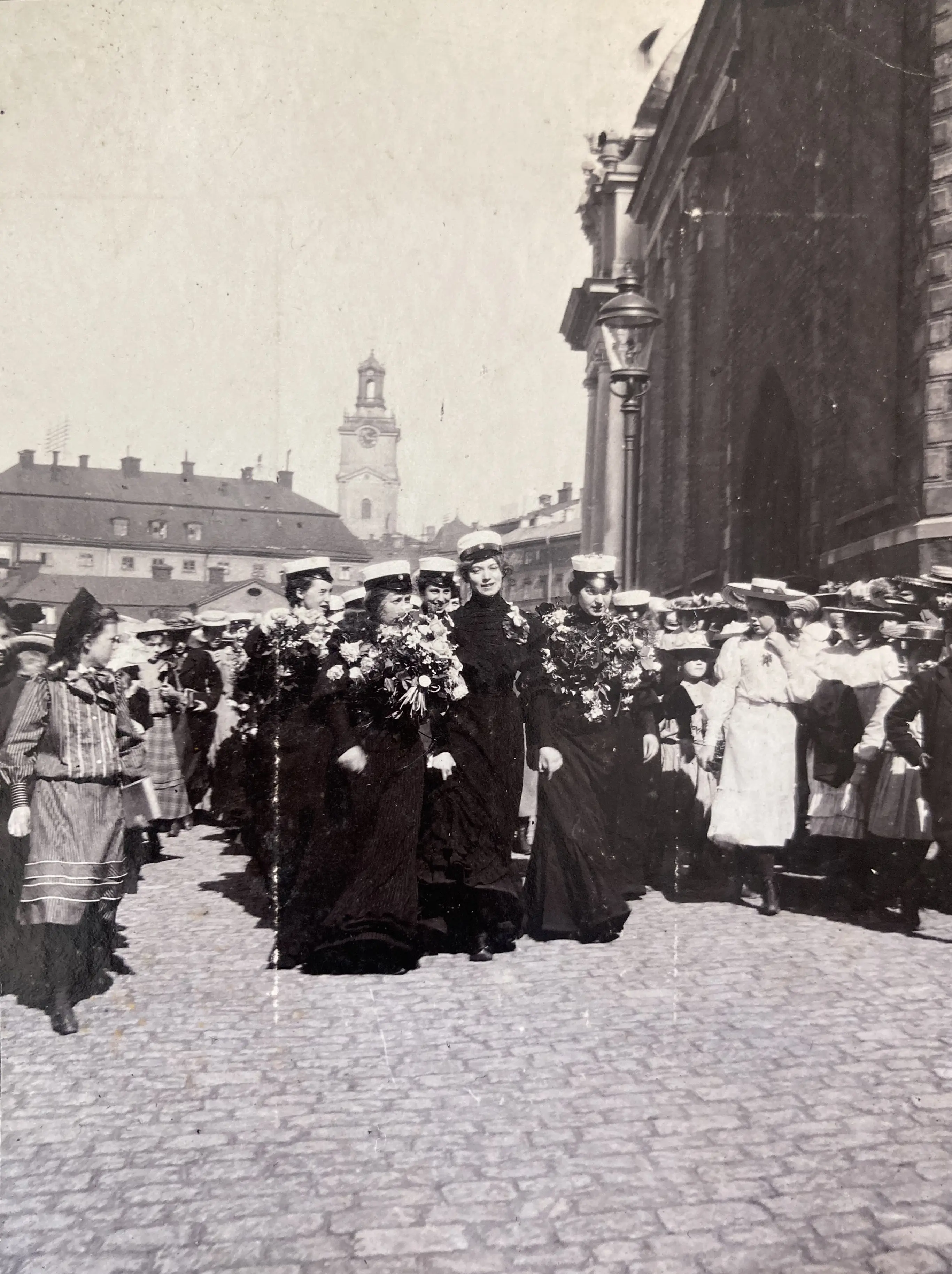 Kvinnliga studenter går i en klunga fram på en kullerstensgata. Gammalt foto i svartvitt/sepia.