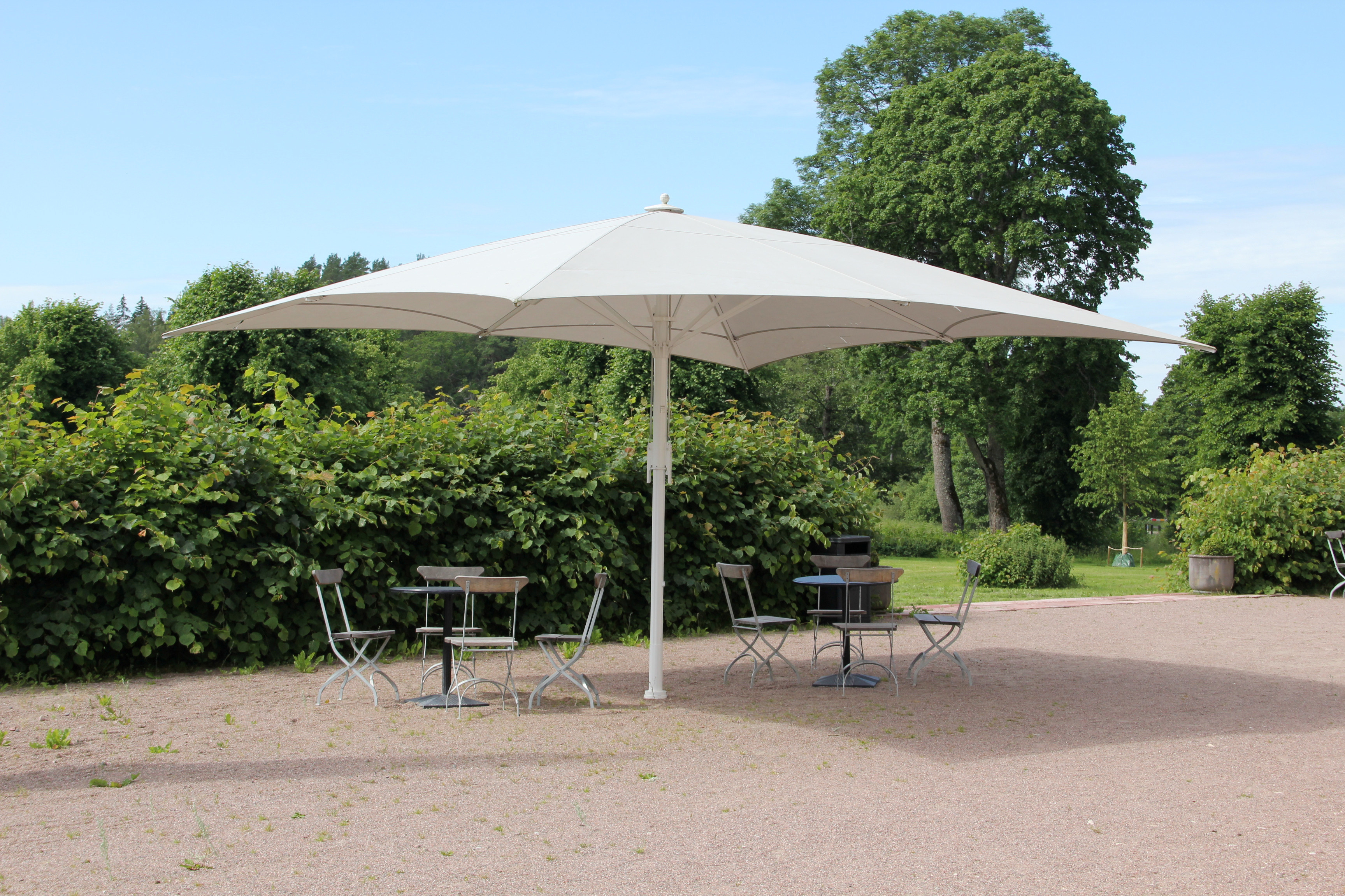 Salsta slottspark. Utemöbler och ett stort parasoll. Sommar och grönska.