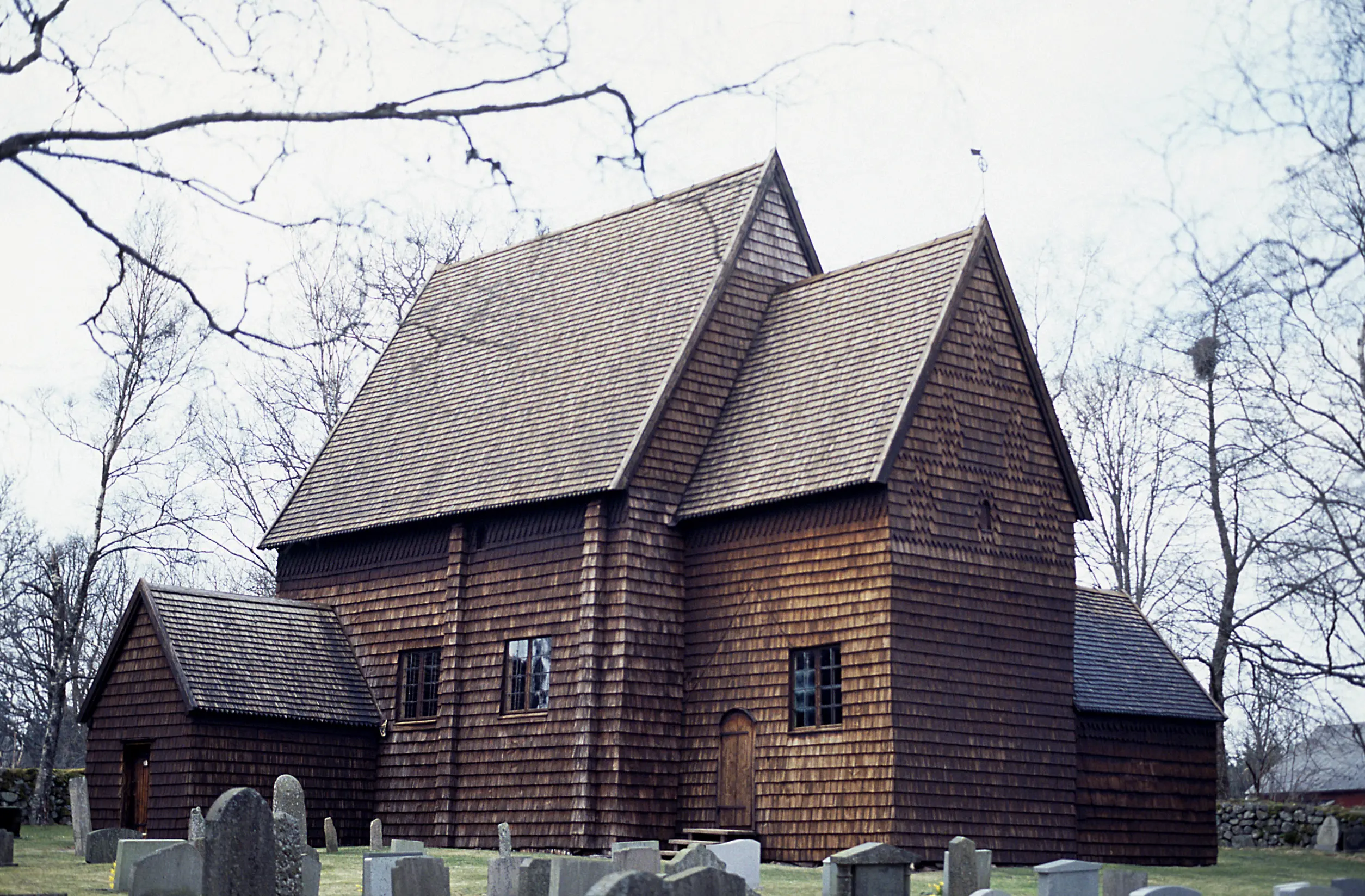 En kyrka i trä. Framför kyrkan finns gravstenar.