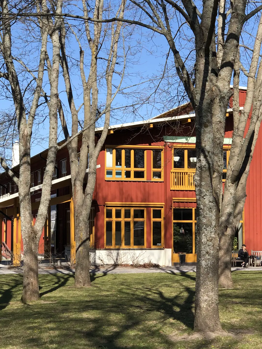 Etnografiska museets röda träfasad med trädstammar i förgrunden.