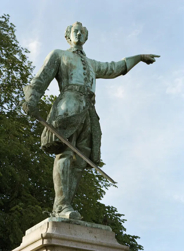 Karl den tolftes staty i Kungsträdgården. Ärgad brons-staty av en man som pekar åt sidan med vänstra handen. I den högra håller han ett svärd.