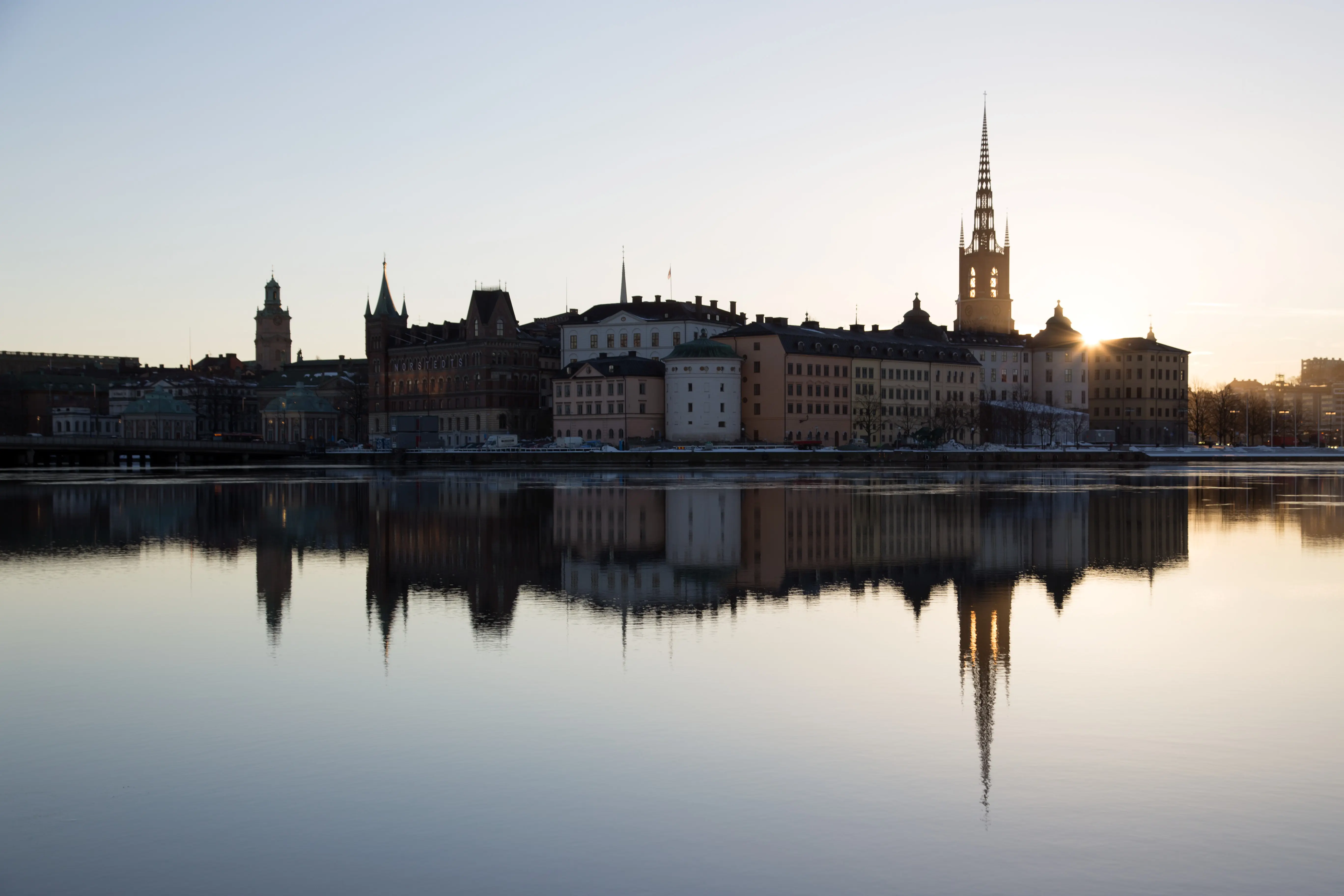 Riddarholmen sett från Stadshuskajen en tidig vintermorgon. Riddarfjärden är stilla och byggnaderna speglas i vattnet.