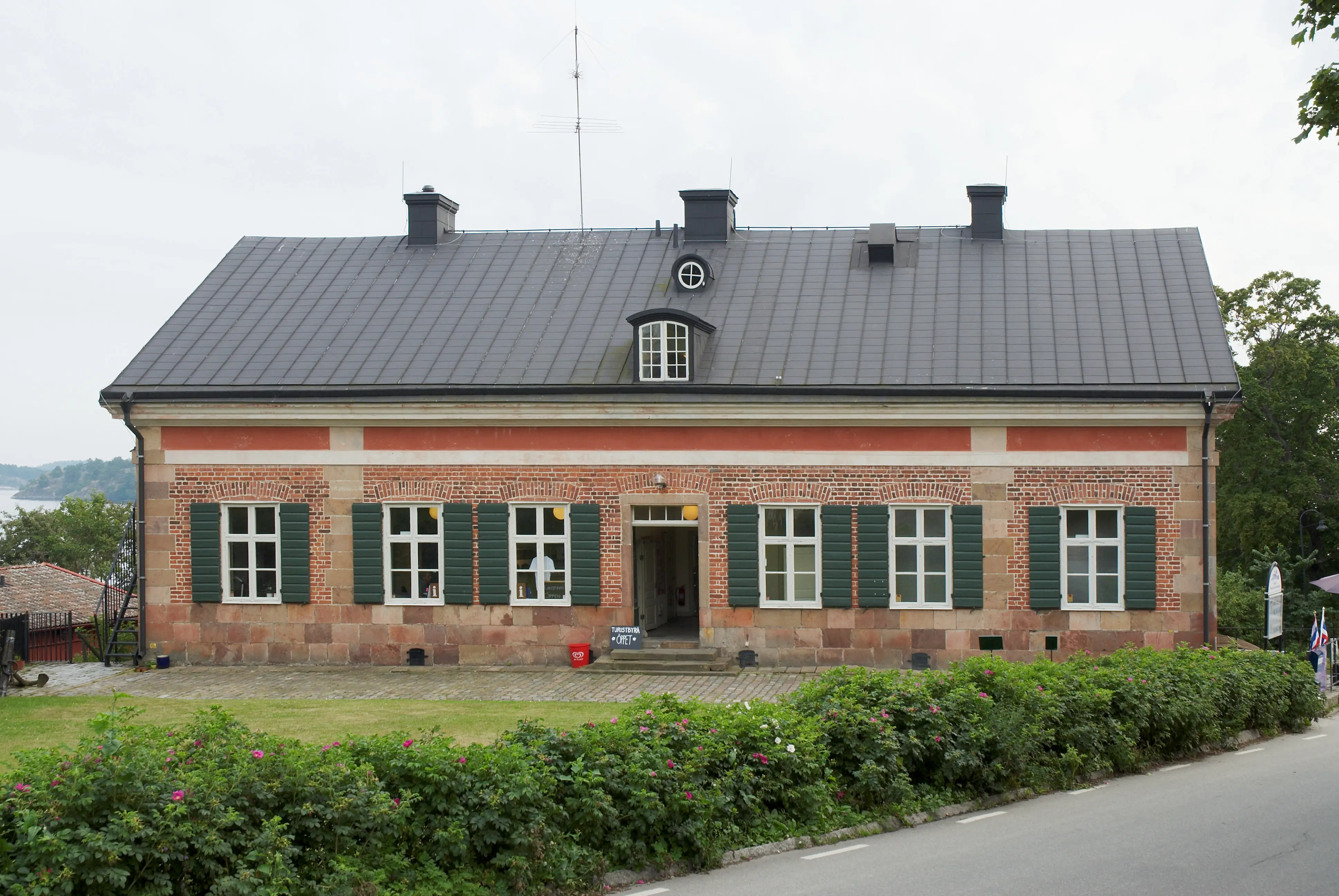 Dalarö tullhusEn tegelbyggnad på stensockel, med gröna fönsterluckor. Det svarta plåt-taket har en tak-kupa.