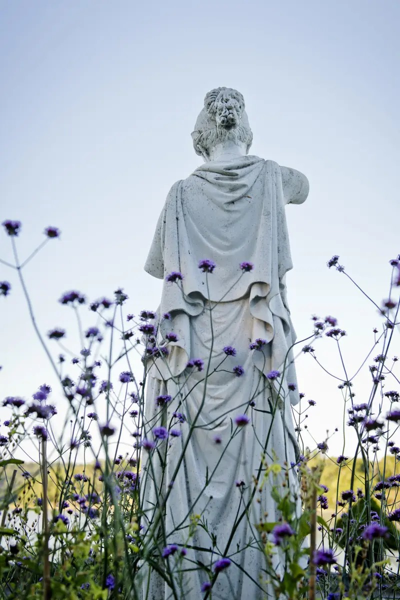 Staty föreställande en kvinna. Lila blommor i förgrunden.