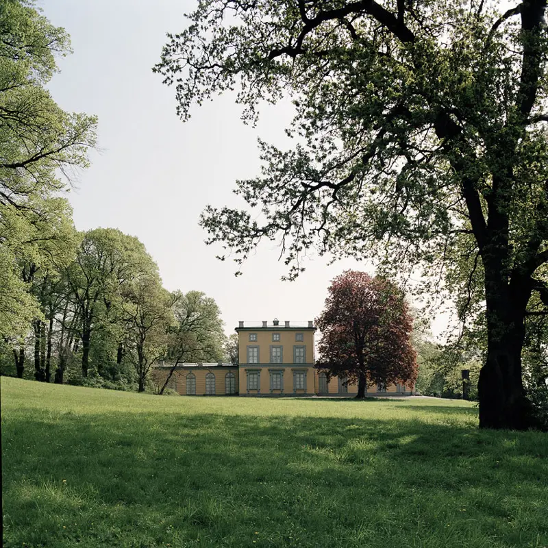 Gustav III:s paviljong omgiven av lövträd och med en gräsyta framför.