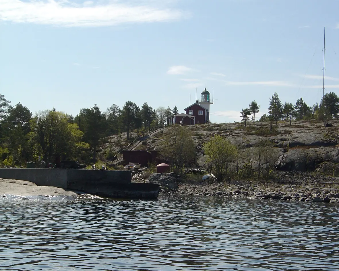 Brämöns fyr och lots-stuga på klippan ovanför hamnen. Ön är bevuxen med tallskog.