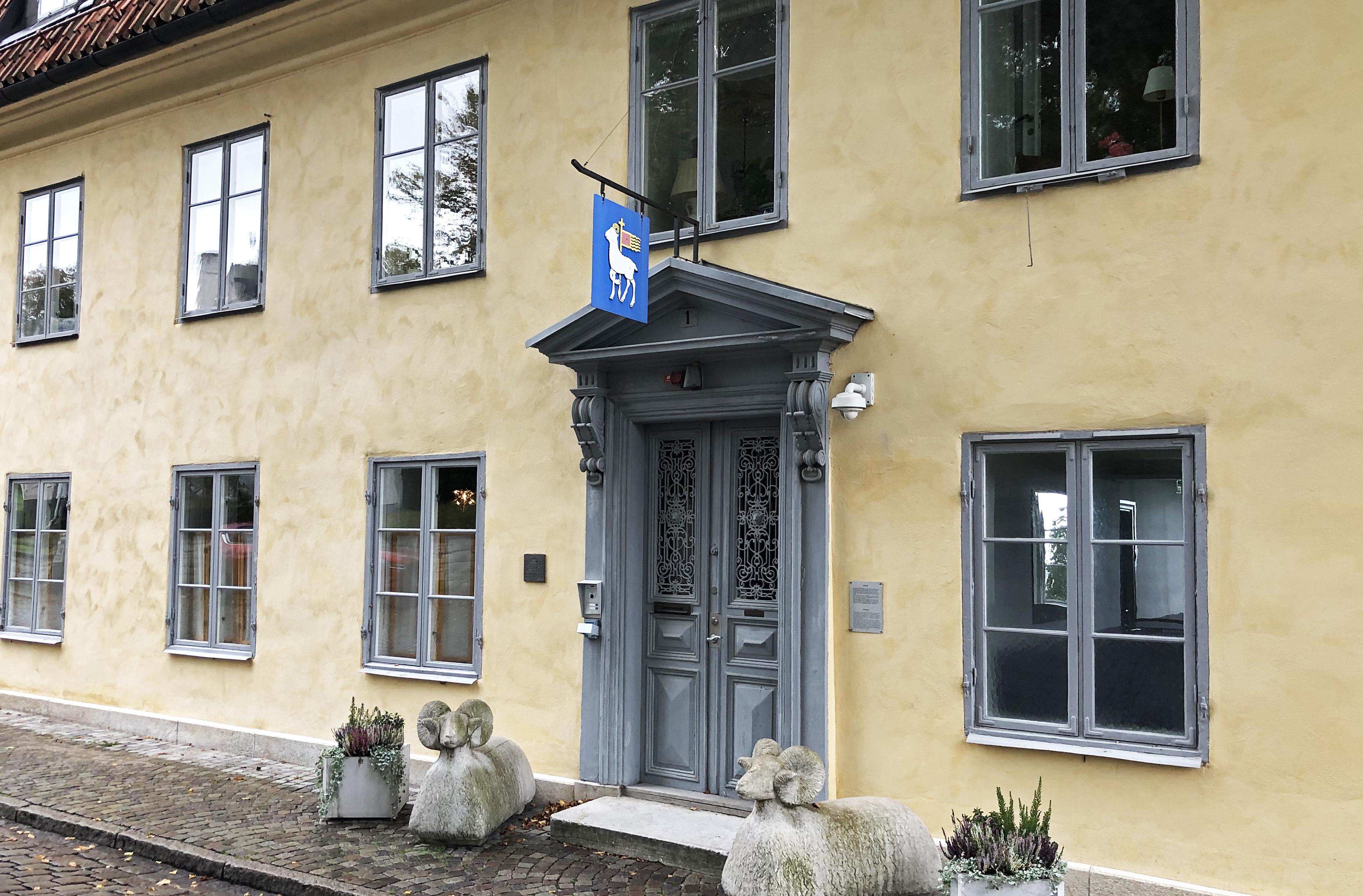 Visby residens, huvudentrén. Fasaden är gulputsad och den sirliga träportalen flankeras av två skulpterade baggar. Höst.
