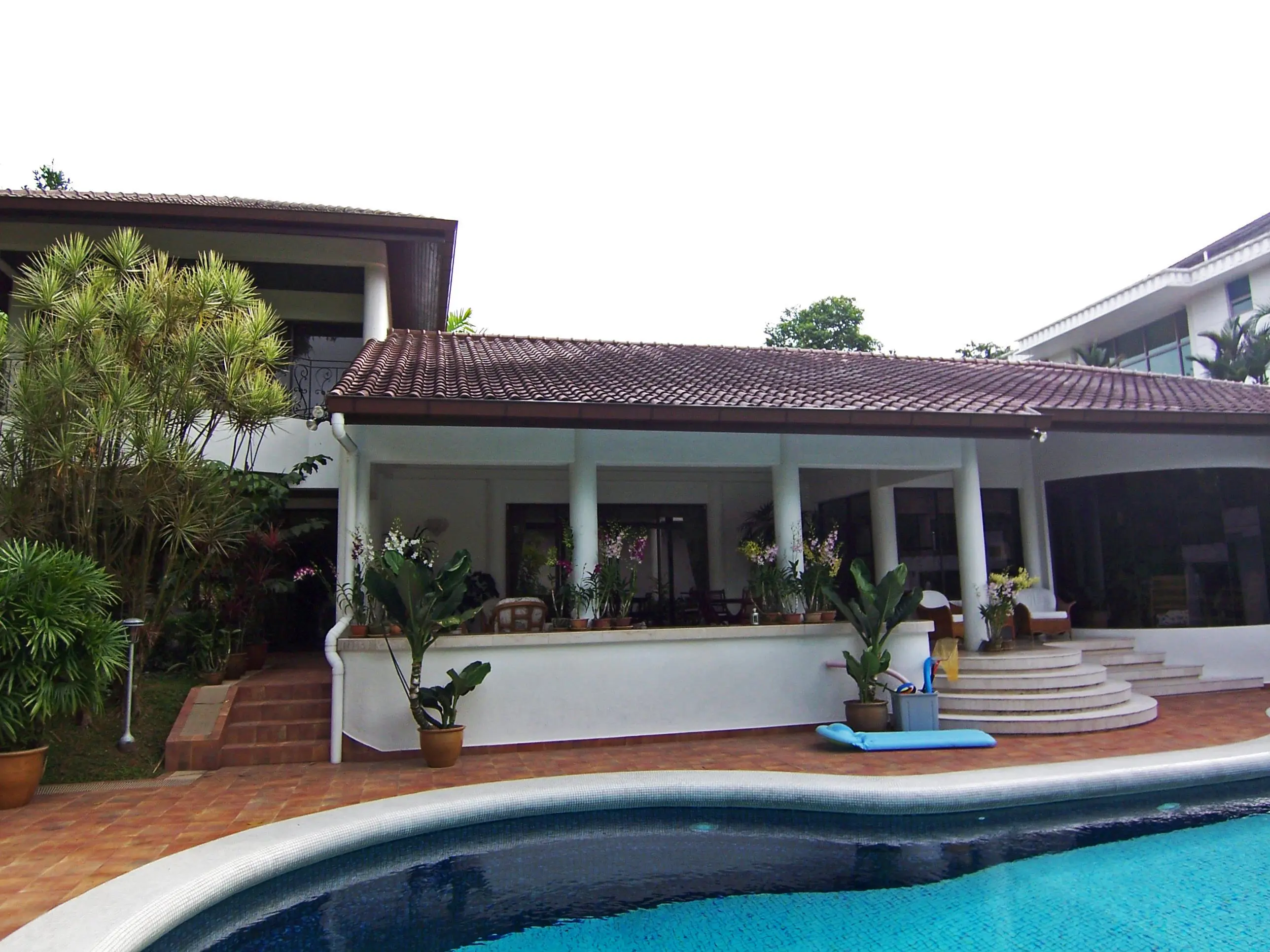 Chefsbostaden, Singapore. Vit tvåvåningsbyggnad med tegeltak. I förgrunden en pool.