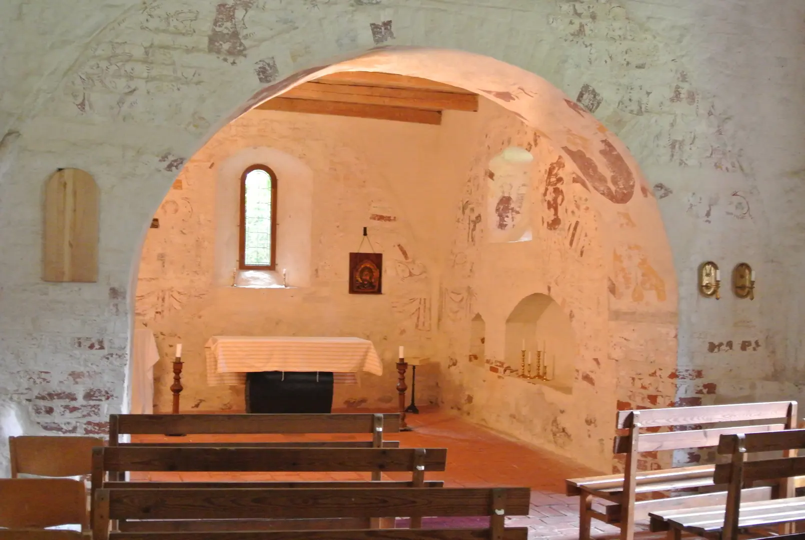 Kyrkans interiör med träbänkar och ett smalt fönster.