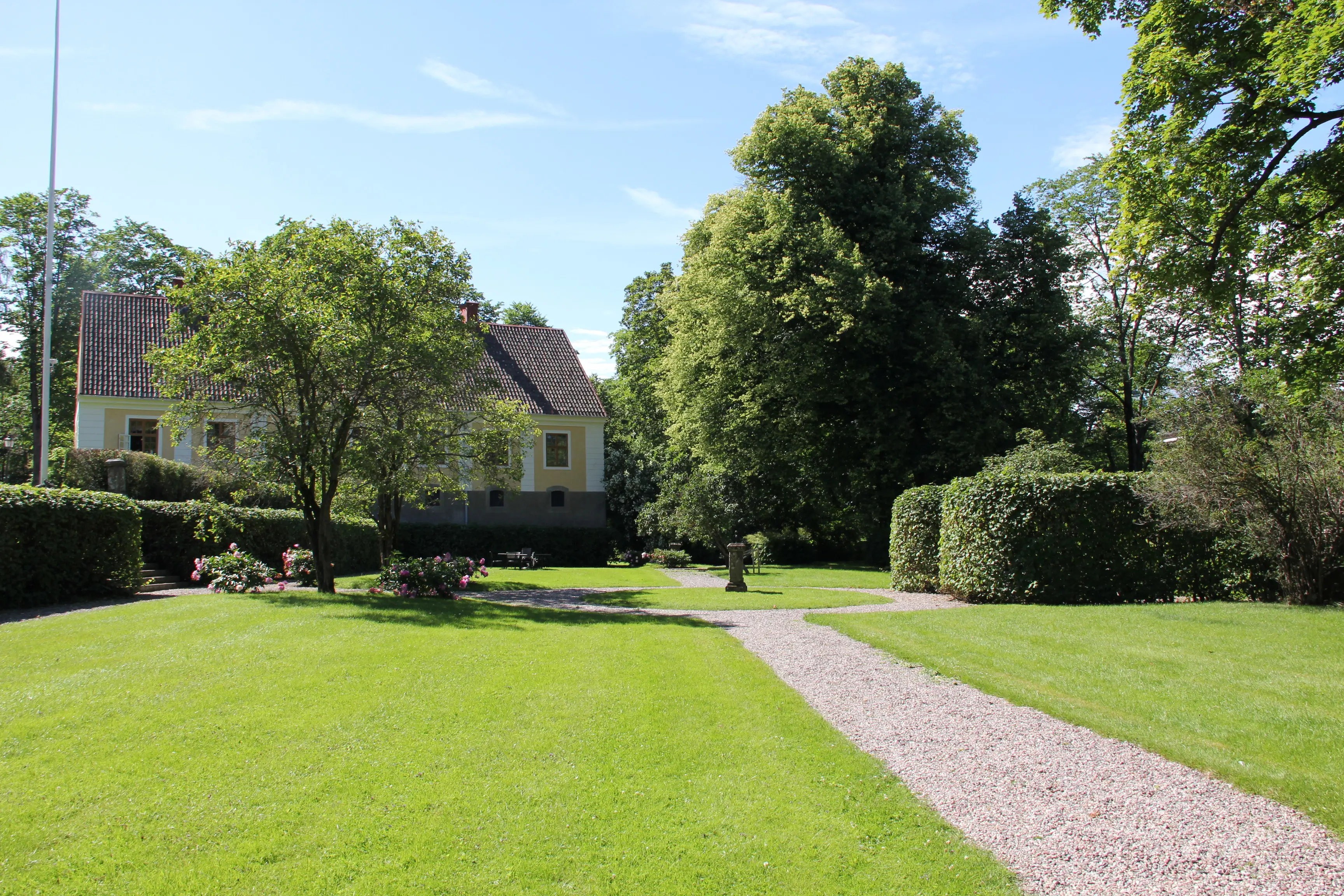 Gävle slottspark. Gräsmattor och grusgångar ramas in av pioner, formklippta buskar och grönskande träd.