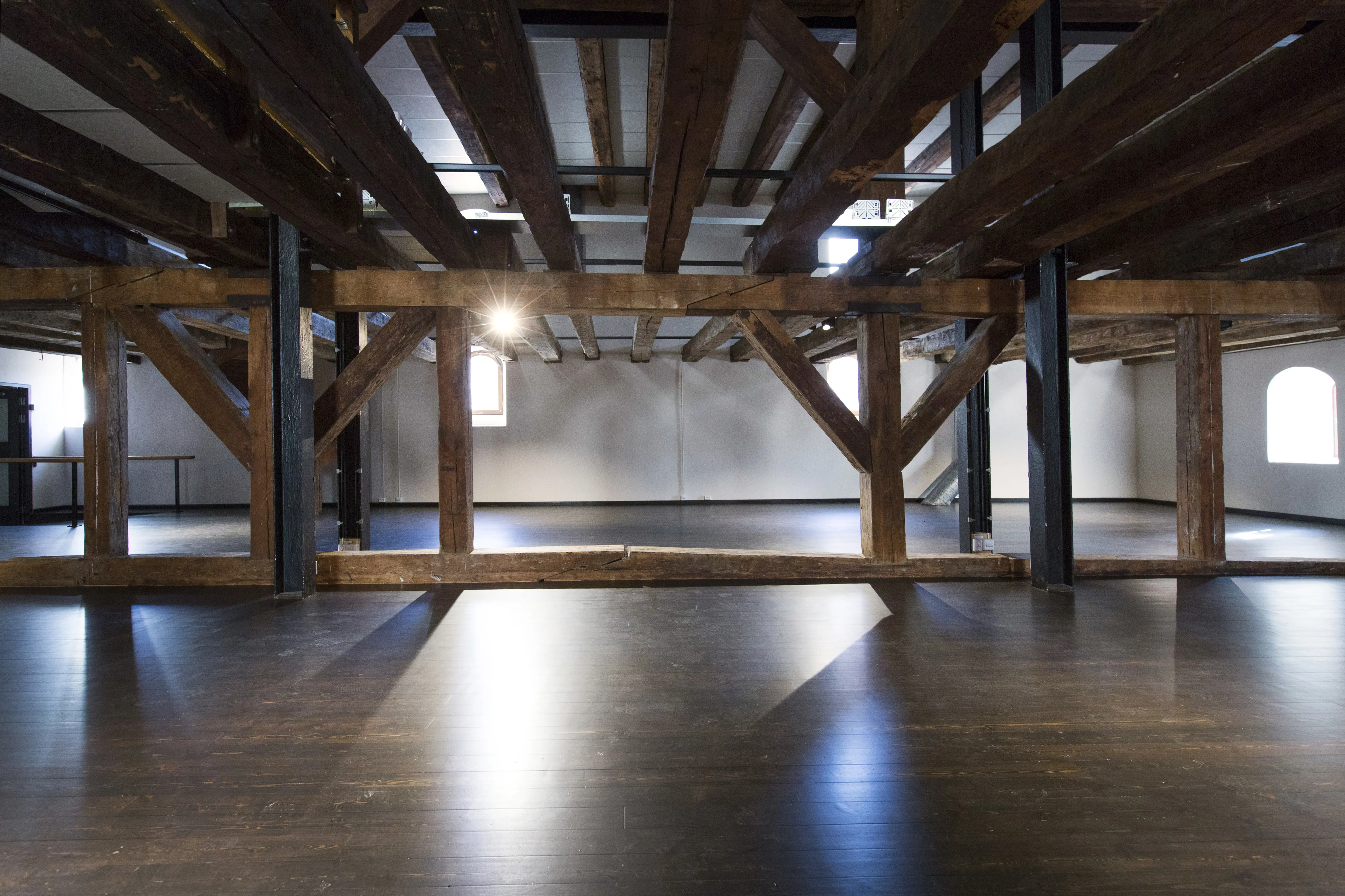Sal med mörkt trägolv. Träbjälkar går både lodrätt från golv till tak och vågrätt i taket.