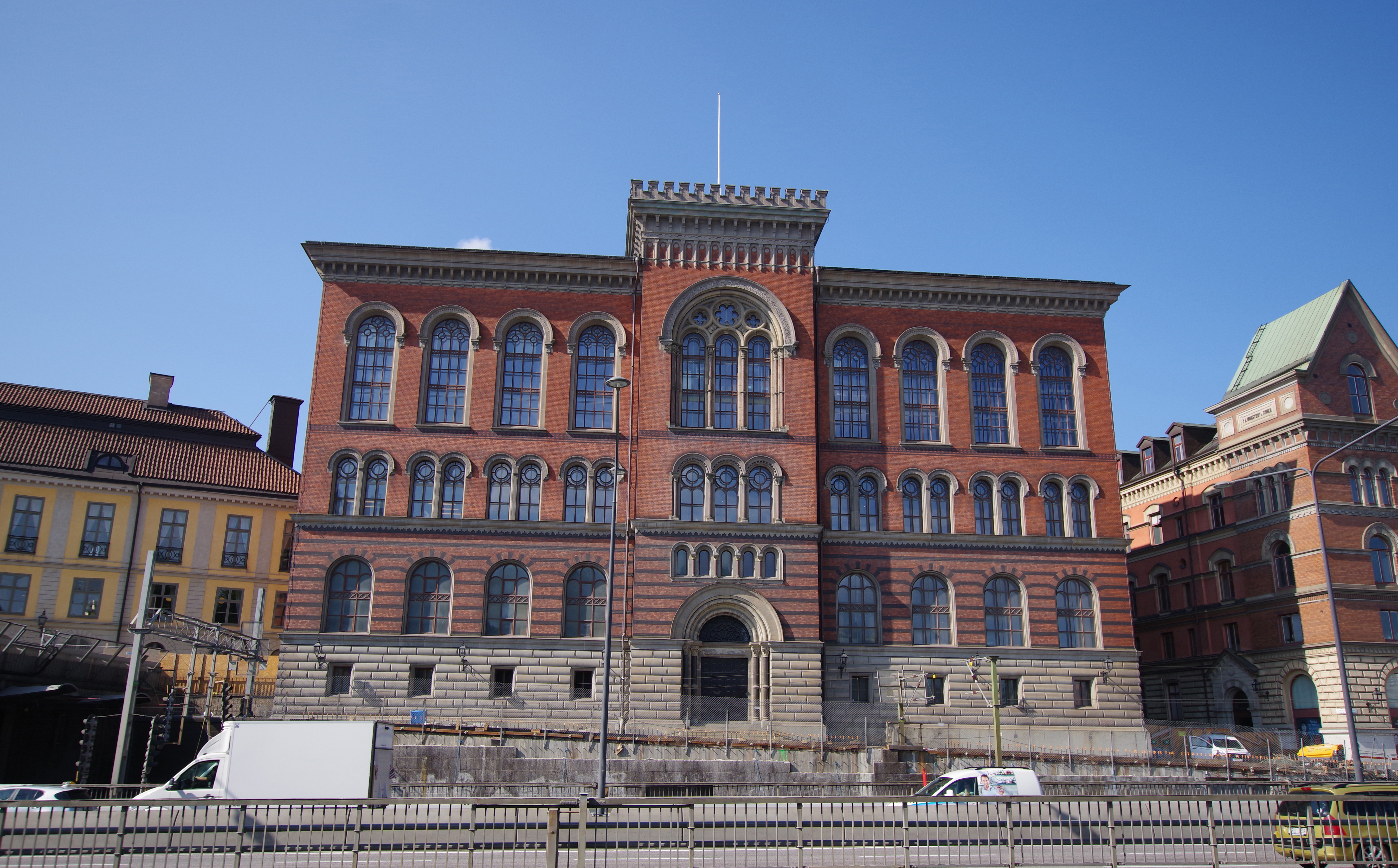 Gamla riksarkivet, fasad mot Gamla stan och centralbron. Röd tegelbyggnad i fyra våningar, med krenelerat mitt-torn och rundade fönster.