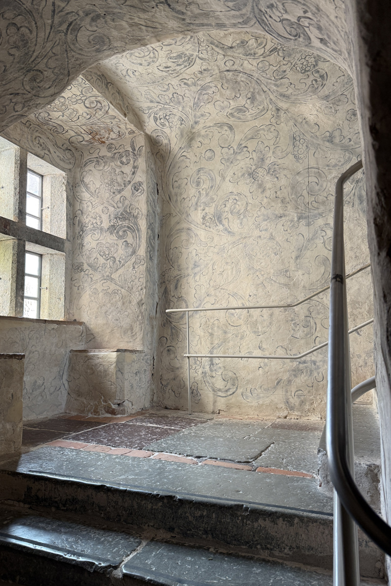 Läckö slott. Avsats med fönsternisch i en stentrappa. Väggar och tak är vita med växtornamentik. Rörformade handledare längs trappan.