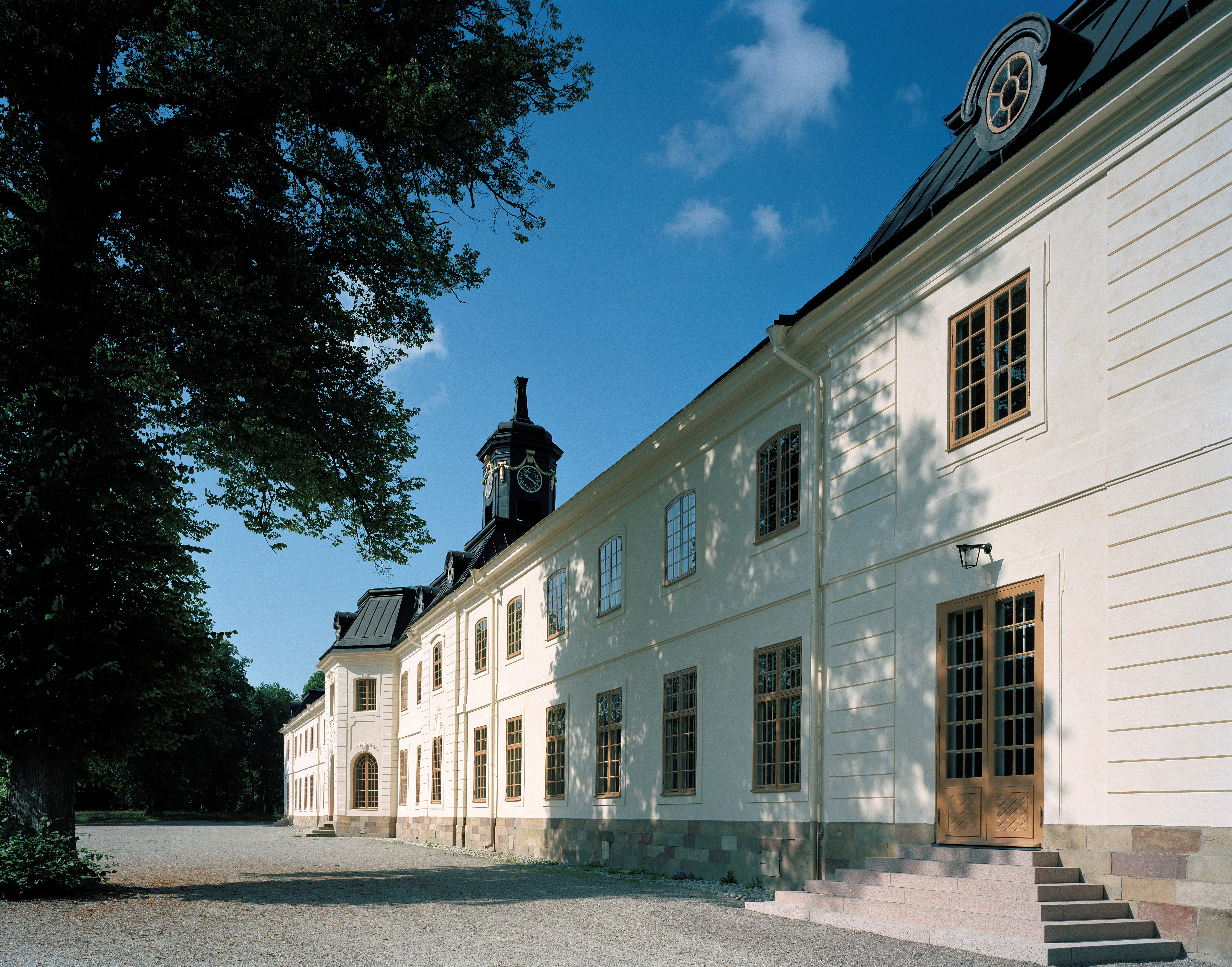 Svartsjö slott. Långsträckt vitputsad tvåvåningsbyggnad i klassicistisk stil. Taket har runda tak-kupor och en lanternin med klocka.