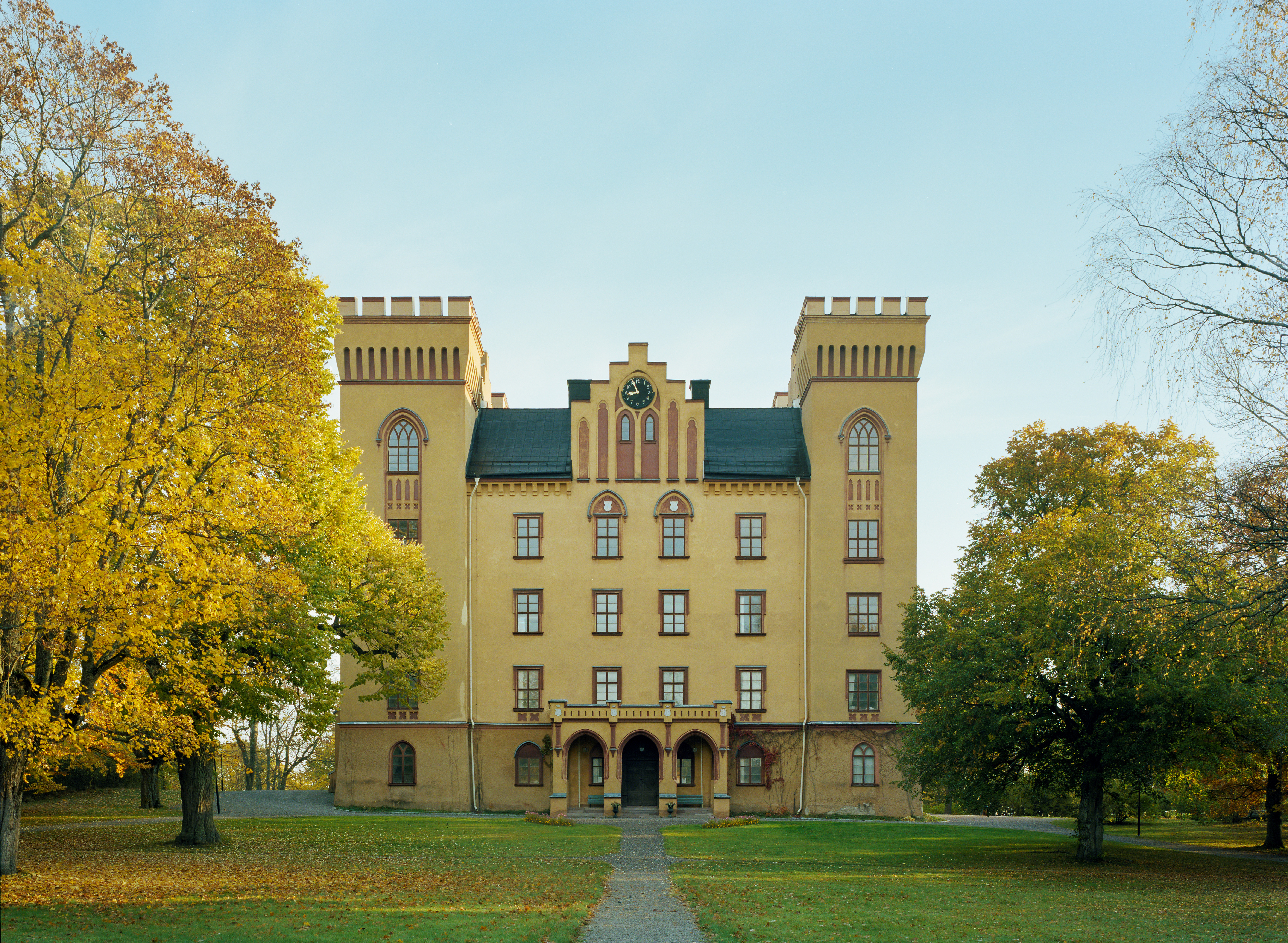 Bogesunds slott. Gulputsad byggnad med liten praktgavel och krenelerade hörntorn. Entrén pryds av en nygotisk portik.