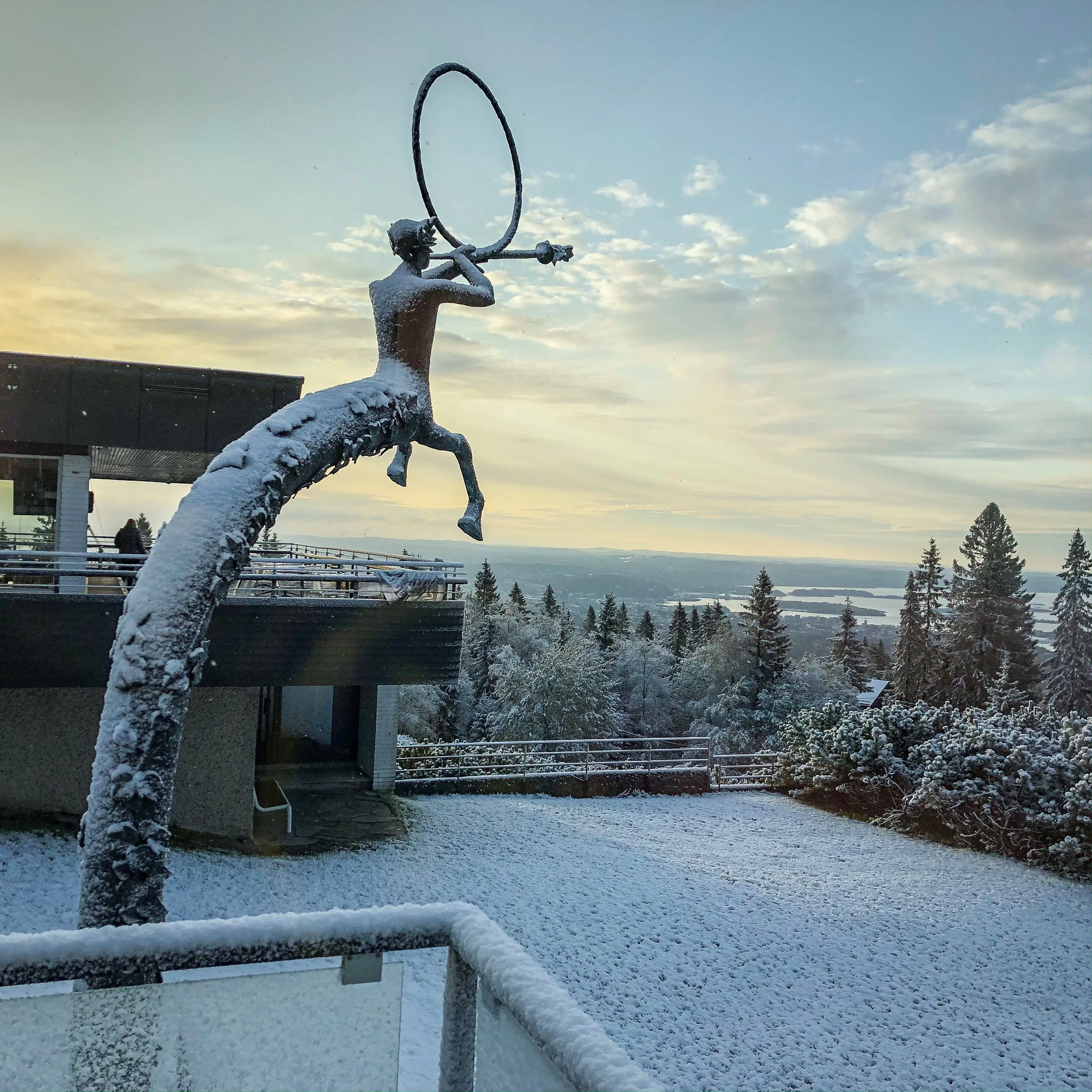 Voksenåsen, exteriör. Utsikt mot Oslofjorden. I för-grunden en skulptur av en horn-blåsande kentaur. Skulpturen, byggnaderna, gräsmattan och granarna är täckta av rim-frost