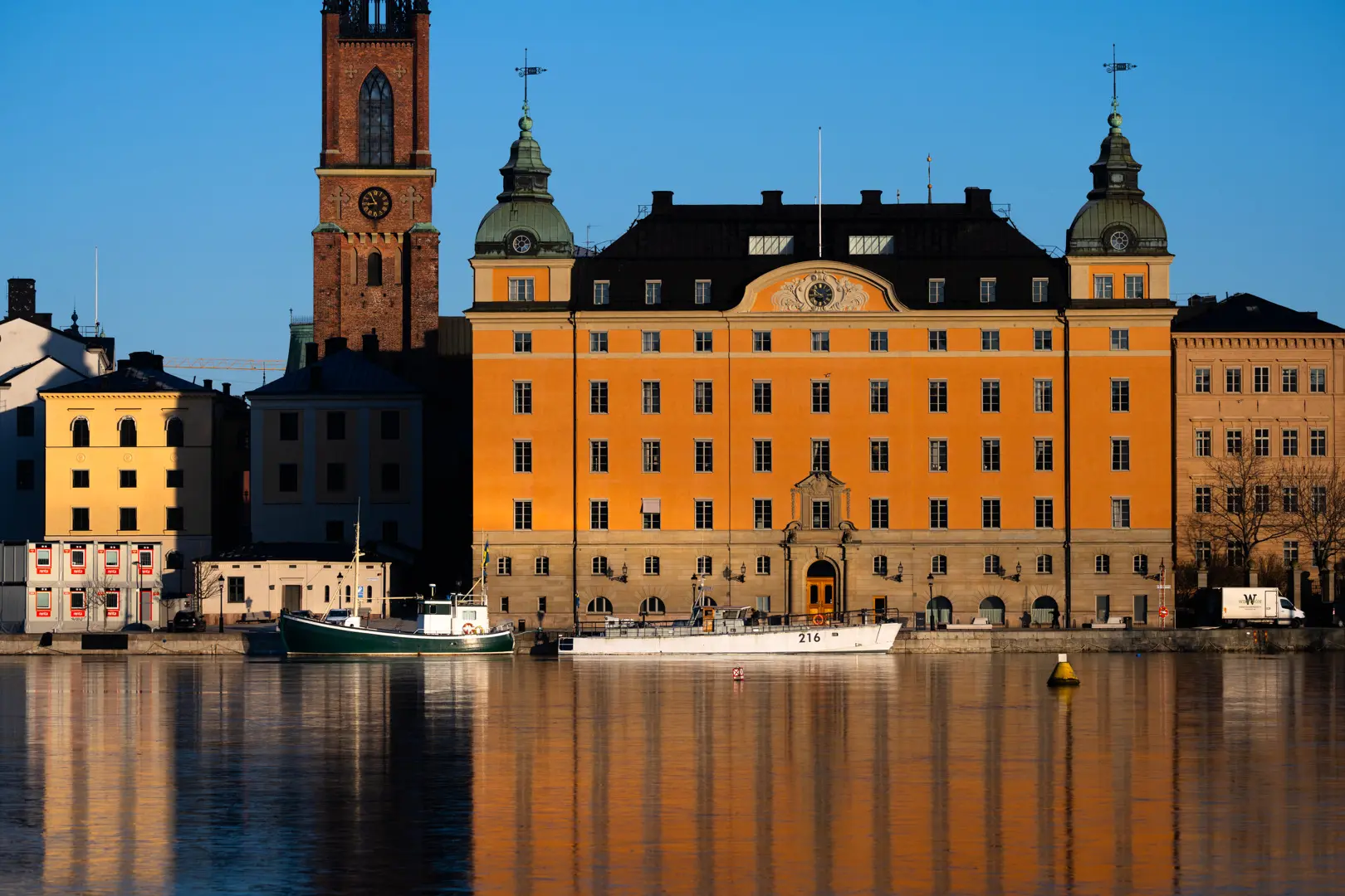 Gamla riksdagshuset på Riddarholmen i morgonljus. Byggnaden speglas i Riddarfjärdens vatten.