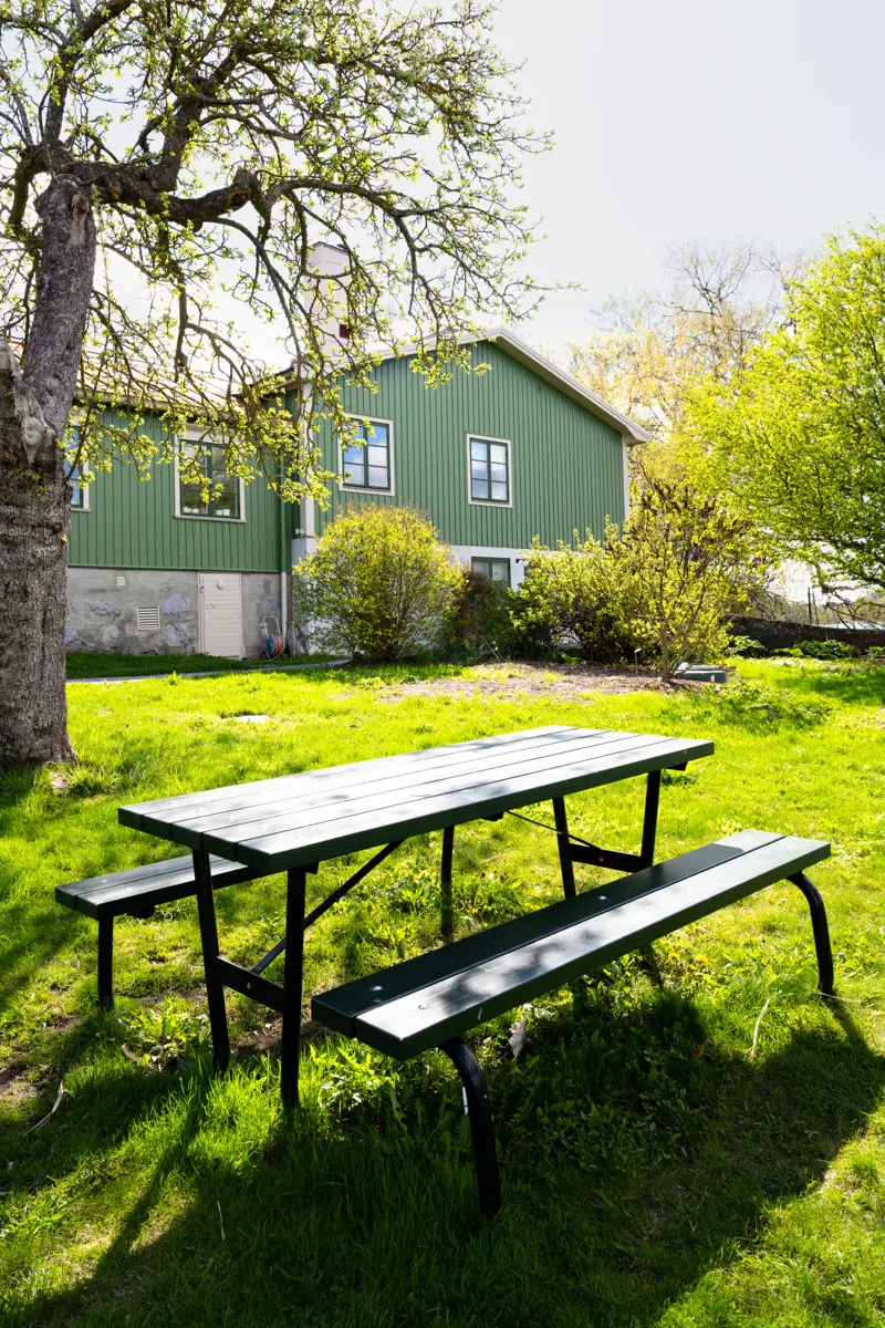 Bergianska trädgården. Grönt trähus. Framför huset står ett bänkbord på en gräsmatta.
