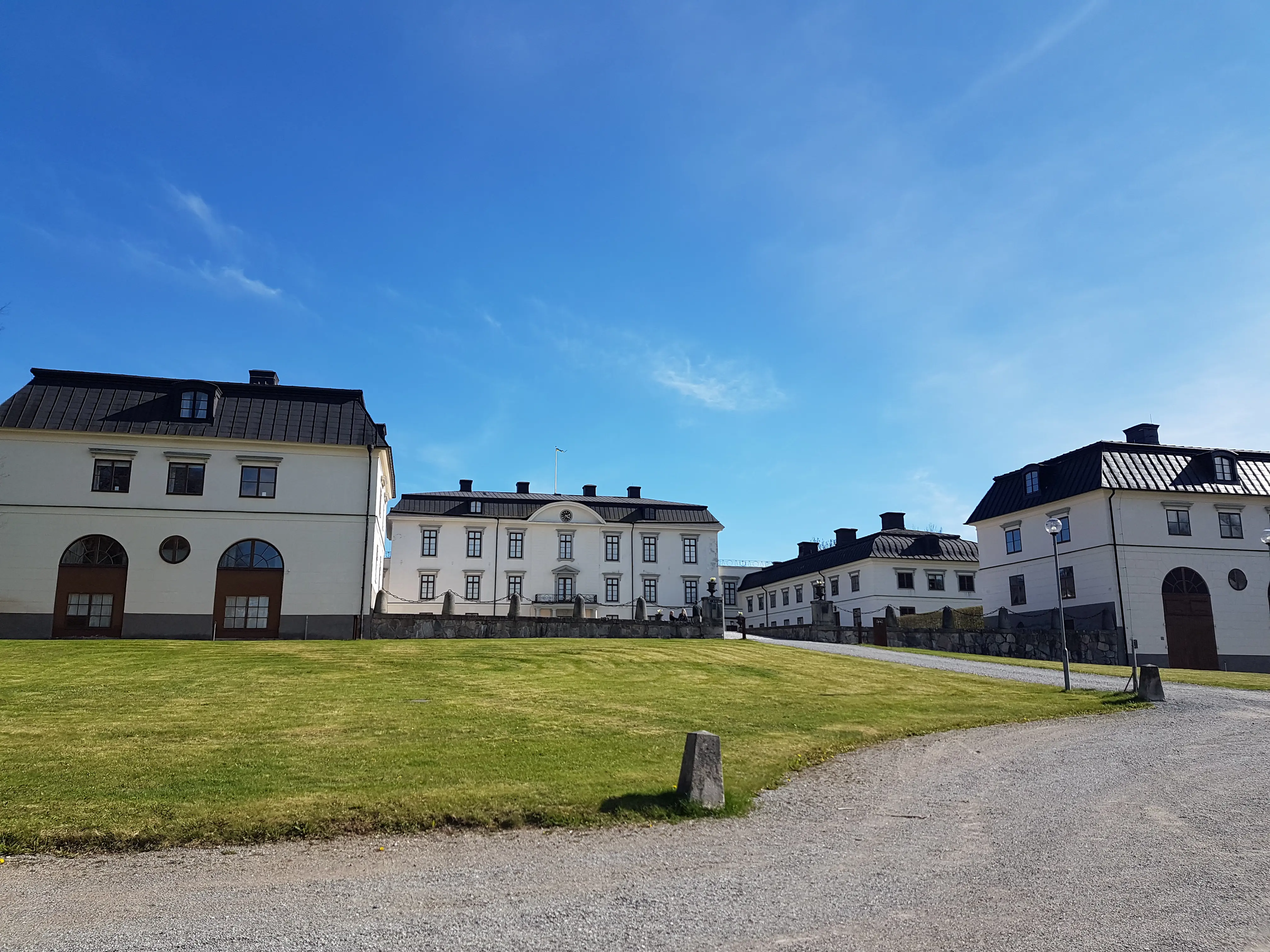 Rosersbergs slott med flyglar. Vitputsade byggnader med svarta plåt-tak.
