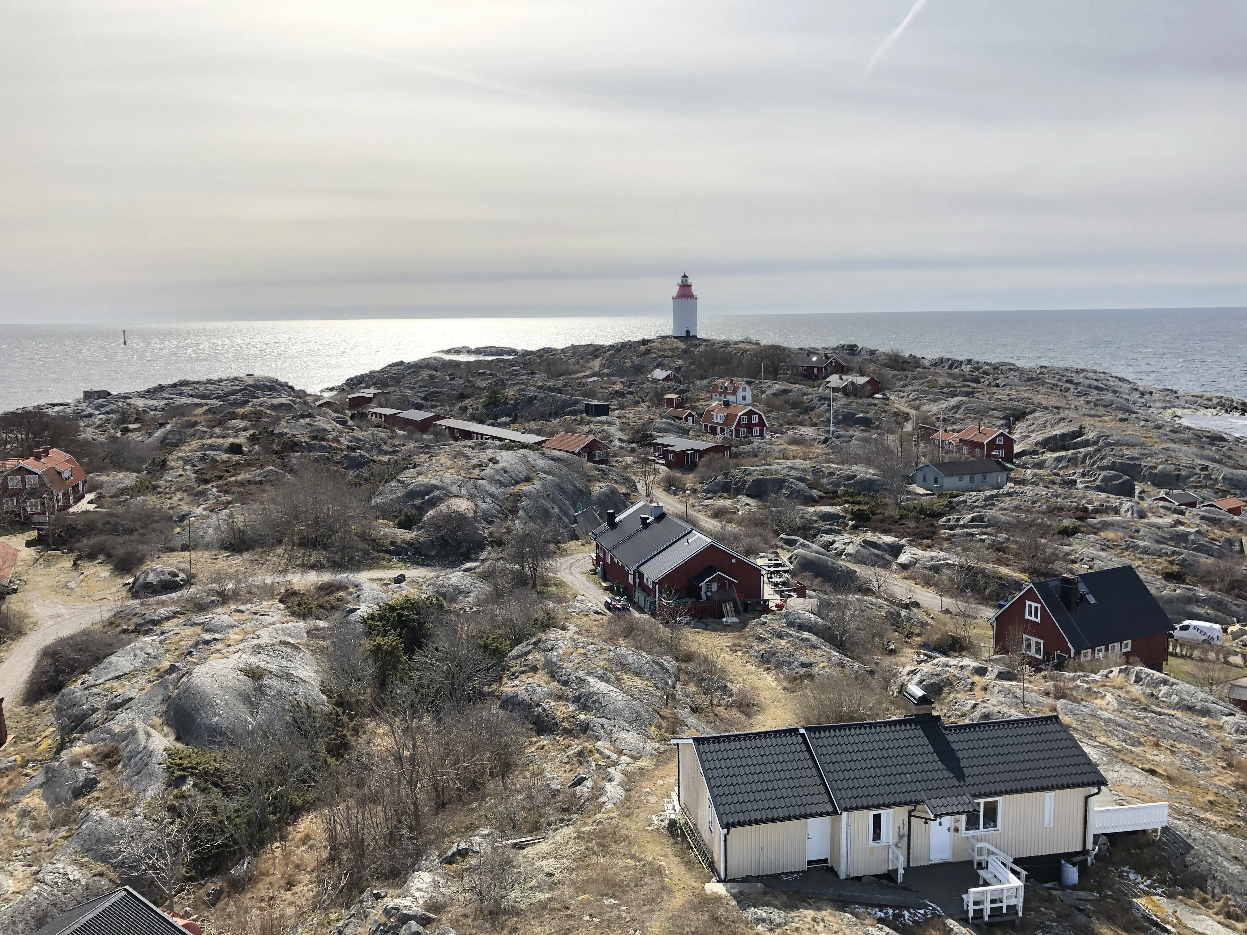 Öja, Stockholms skärgård. Röda och gula trähus av blandad ålder och storlek. Längst bort fyren Landsorts vita torn och utsikt mot Östersjön..