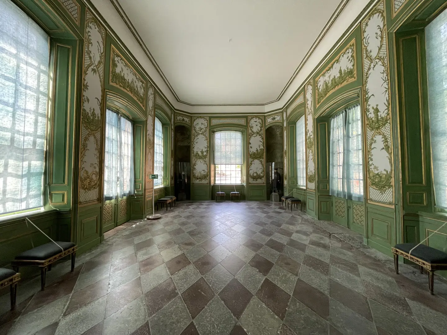 Sal i Kina slott med dagsljus genom tunna gardiner i stora fönster. Väggarna är gröna och vita med målade växtmotiv.