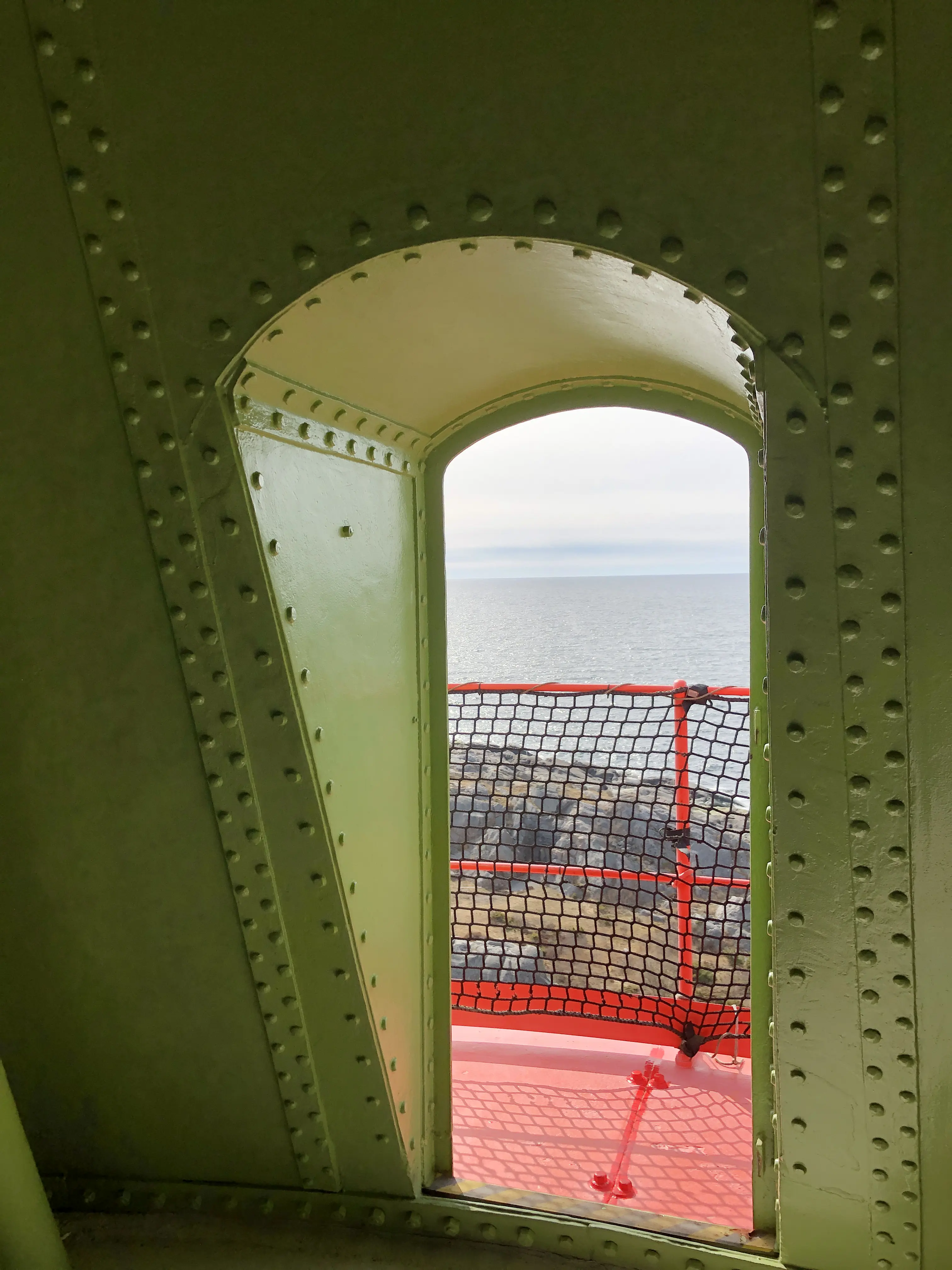 Inuti den koniska plåt-toppen på fyren Landsort. Genom en dörröppning skymtar havet och klipporna.