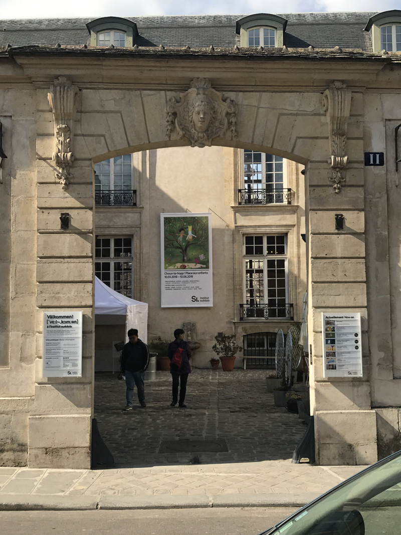Porten till Svenska institutet i Paris sedd från gatan. Genom öppningen syns palatset och ett par besökare på innergården.