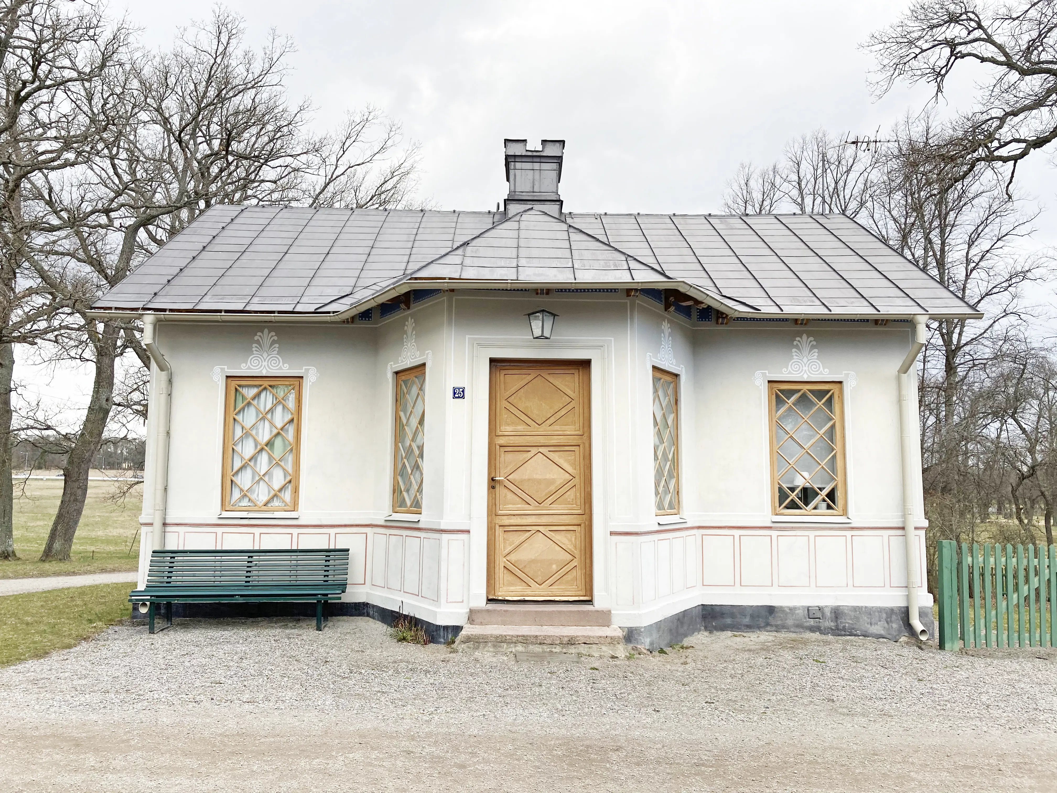 Grindstugan, Drottningholm. Ett vitt litet hus med dekorativ fasadmålning. Fönstren har diagonal spröjs och trädörren har diagonala speglar.