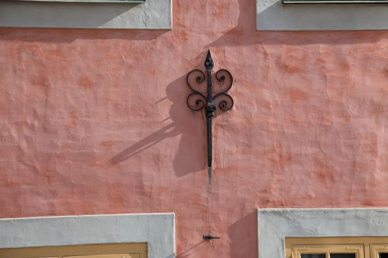 Närbild av ankarslut i sidljus som kastar en skugga på den rosa fasaden.
