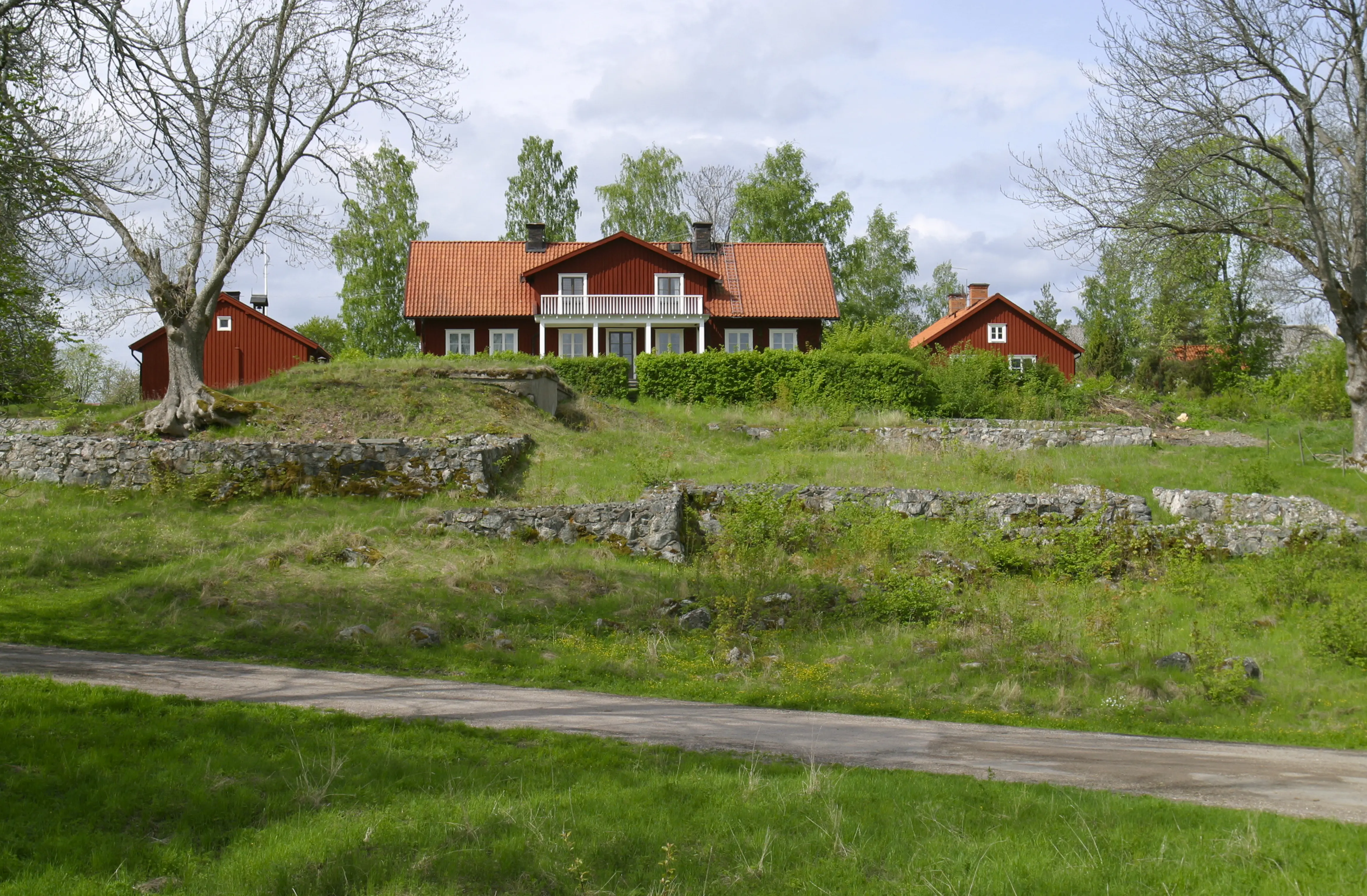 Kungsbergs mangårdsbyggnad med flyglar. I backen framför gården syns resterna av Vårfruberga klosterruin. Vår och grönska.