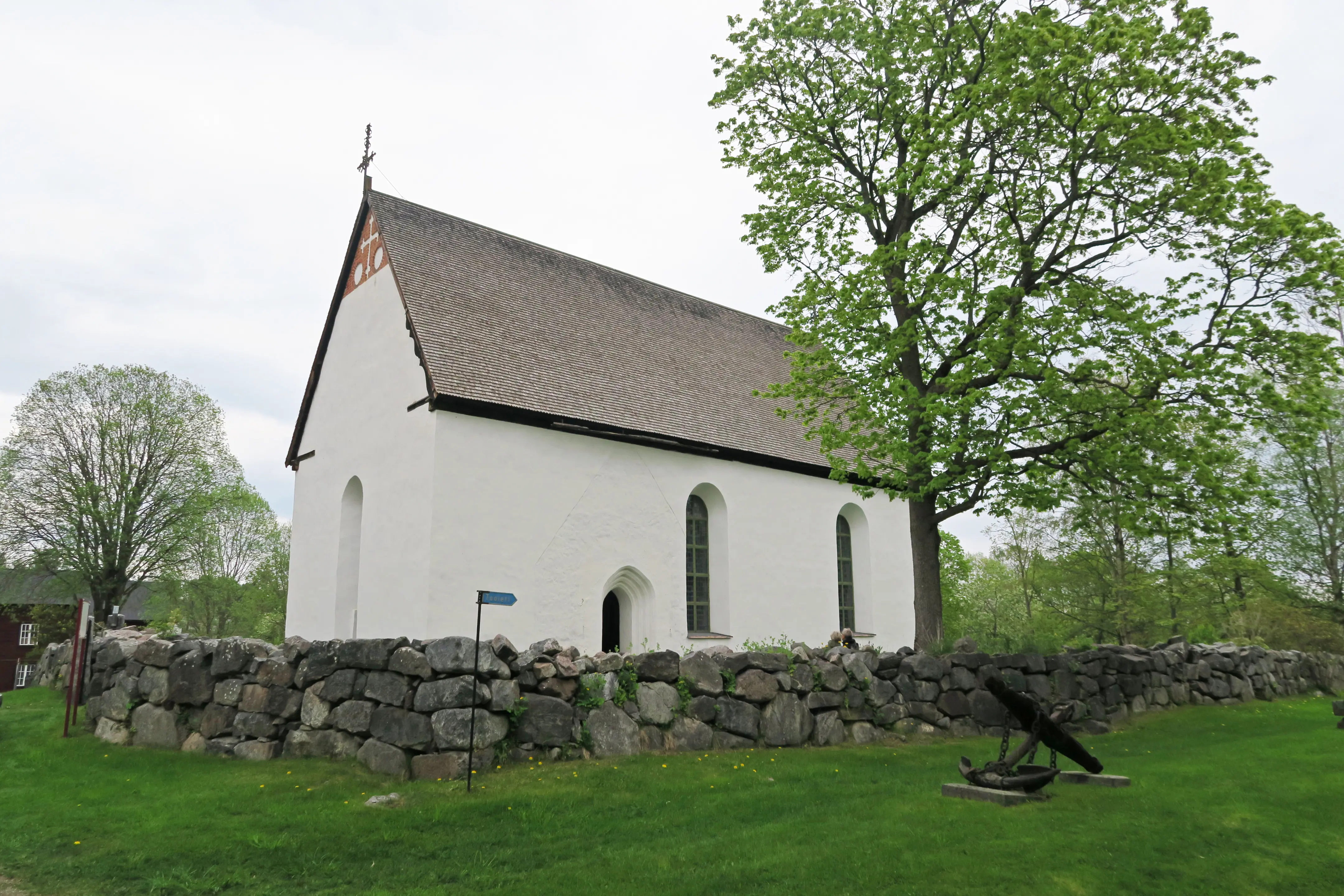 Enångers gamla kyrka. En enkel medeltida kyrka utan torn. Vitputsad med spåntak. Vår och grönska.