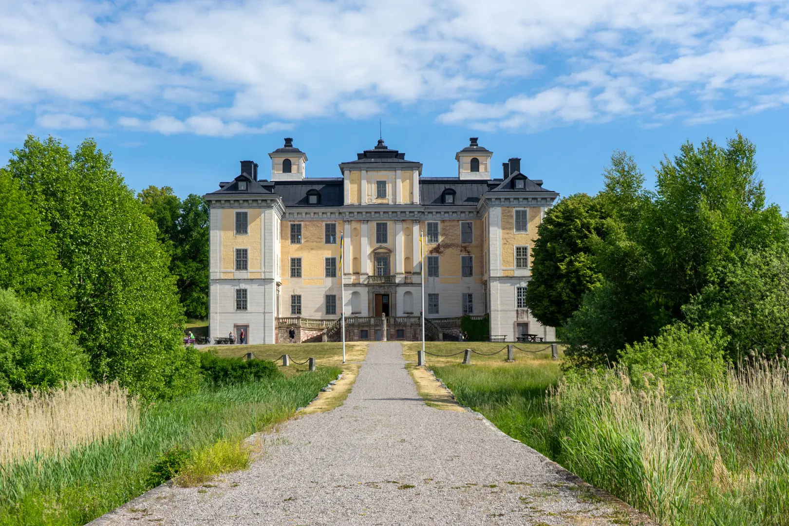 Mälsåker slott under klarblå himmel omgiven av gröna träd och en lång grusgång