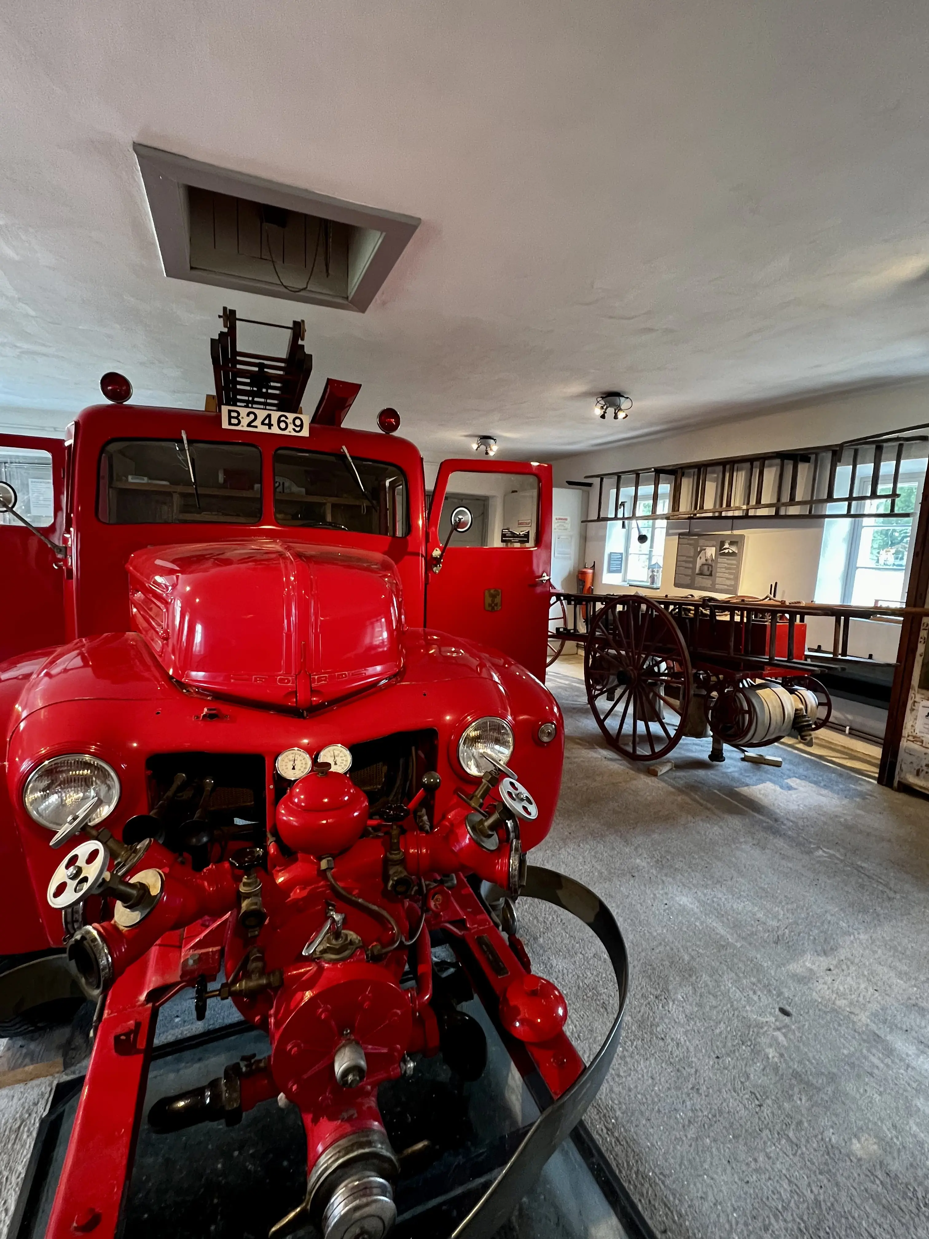 Interiör från spruthuset på Tumba bruk. En knallröd gammal brandbil och annan äldre brandkårsutrusning är utställda.