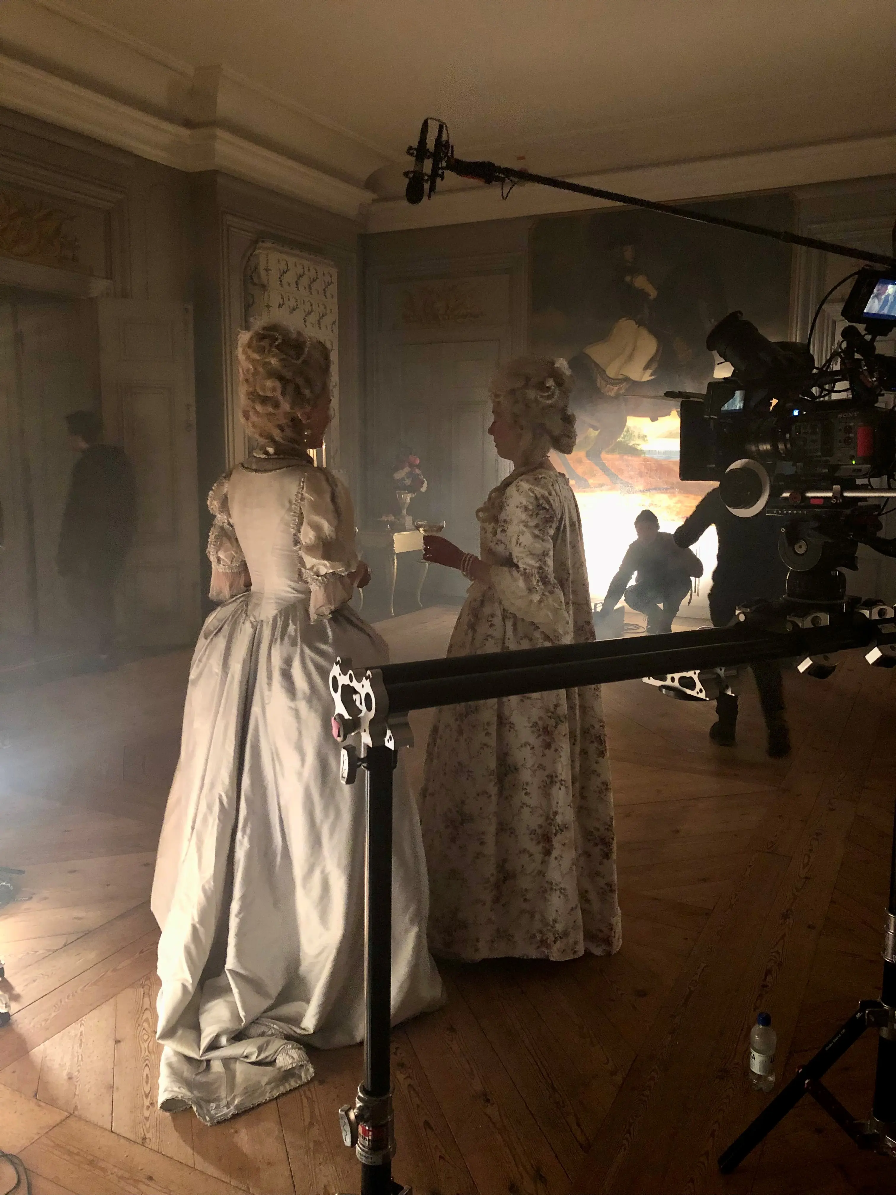 Filminspelning i en salong på ett slott. Två personer i historisk dräkt står bland filmutrustning.