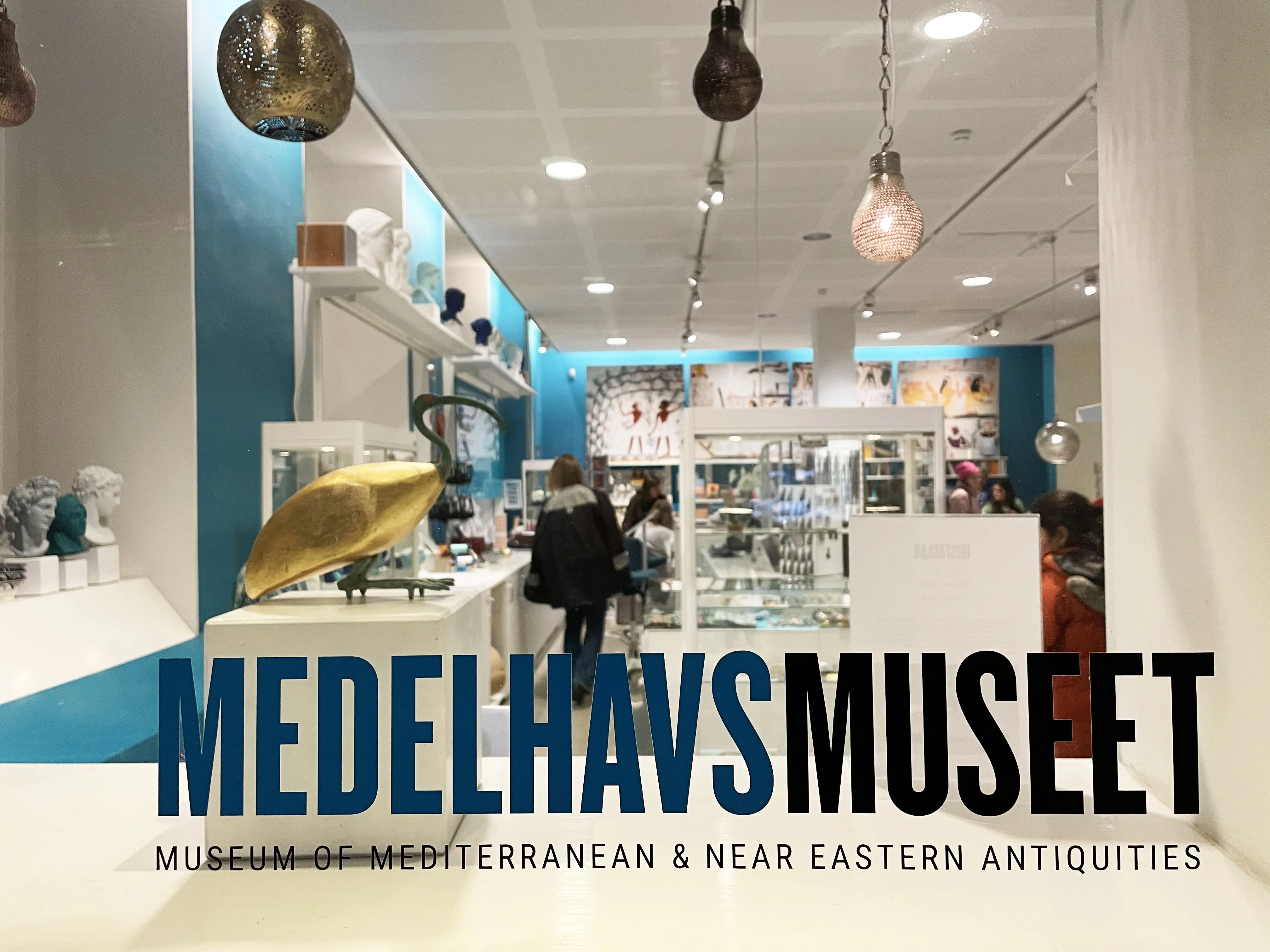 Medelhavsmuseet. Skyltfönster till museibutiken, inredd i vitt och blått. På fönstret står museets namn på svenska och engelska.