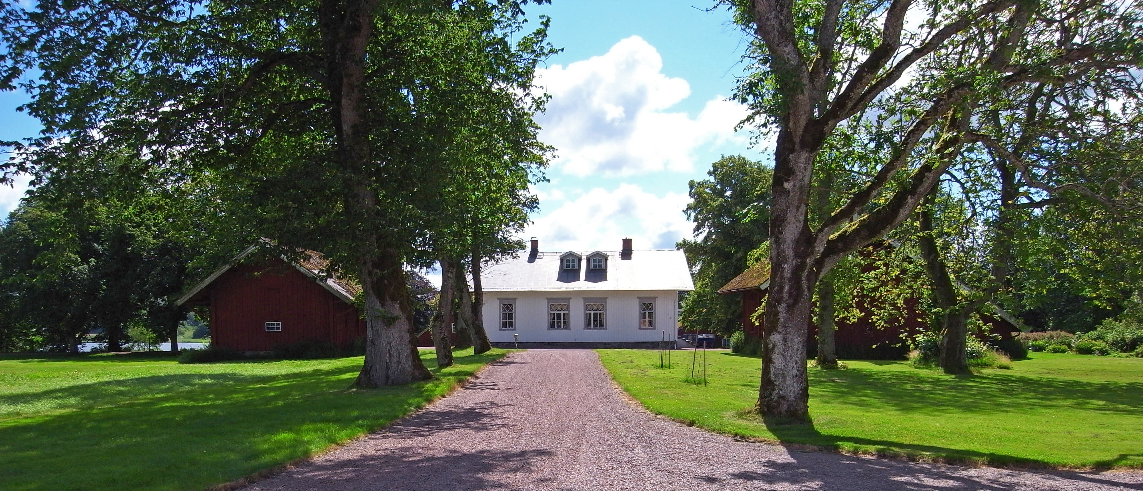 Kastellegården. En kort allé leder fram till den lilla vita huvudbyggnaden, flankerad av två låga flygel-byggnader i röd-målat trä