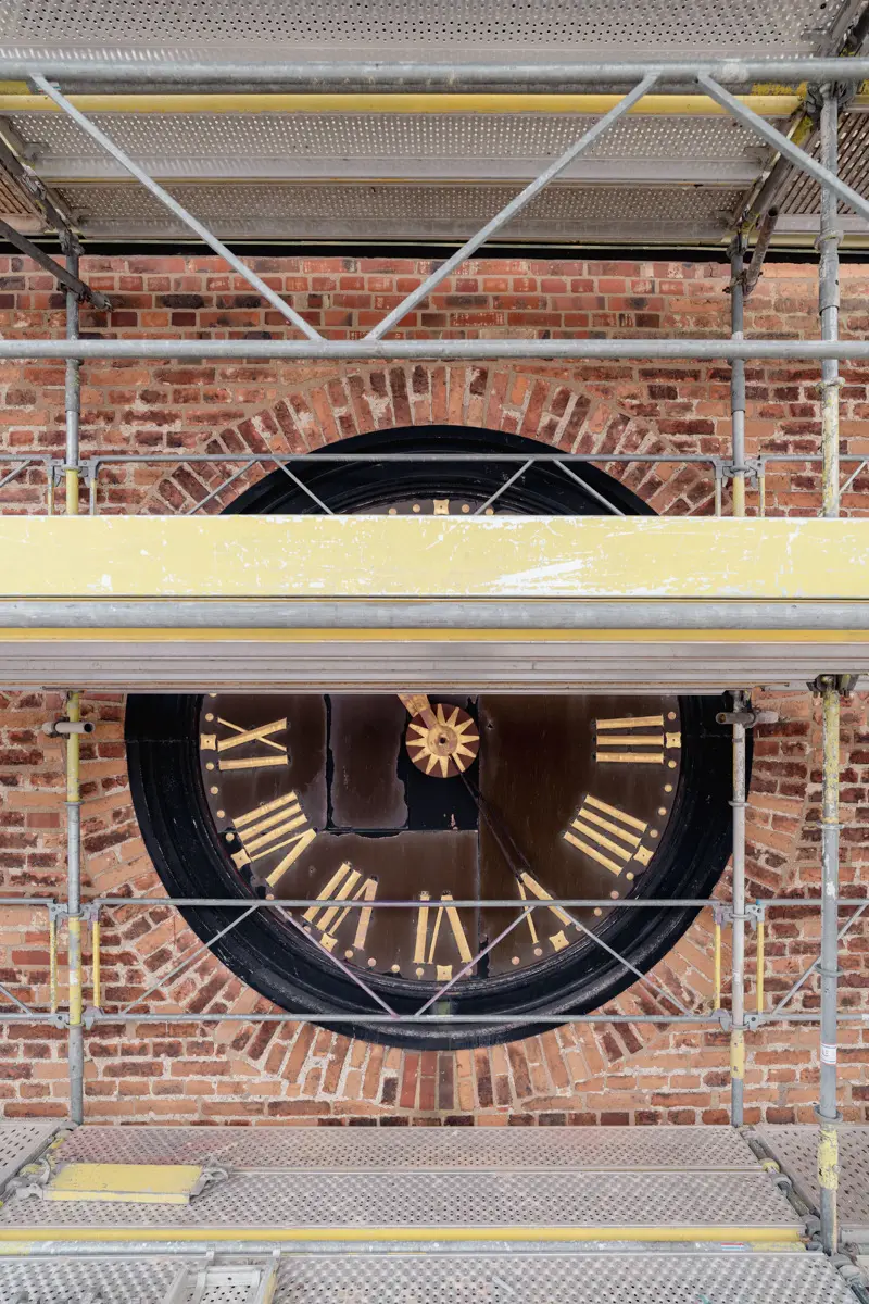 Klocktavla på en tegelvägg, delvis täckt av byggnadsställningar