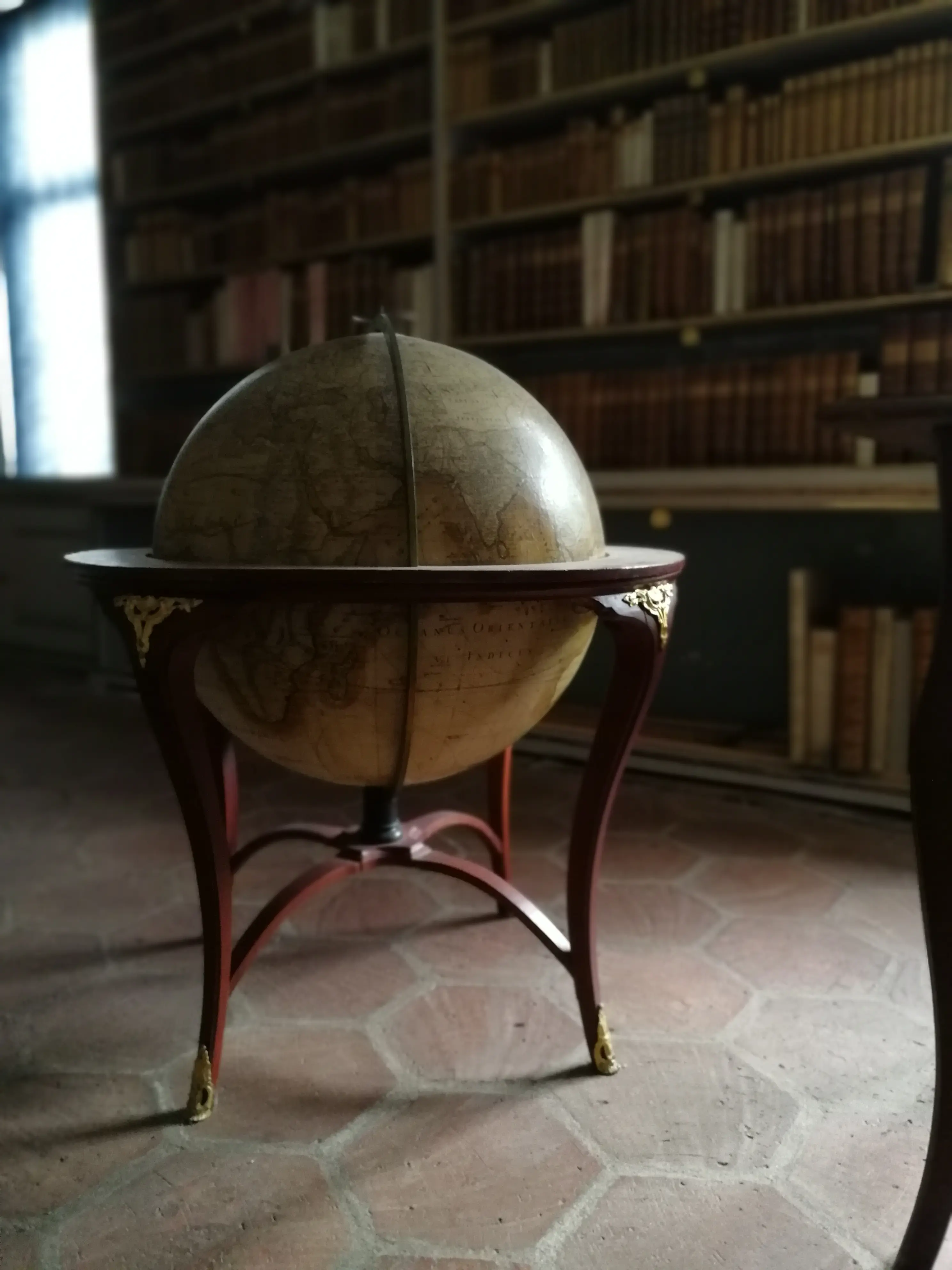Biblioteket vid Lövstabruks herrgård. Interiör med sexkantigt tegelgolv, väggfasta bokhyllor och en jordglob i ett sirligt trästativ.