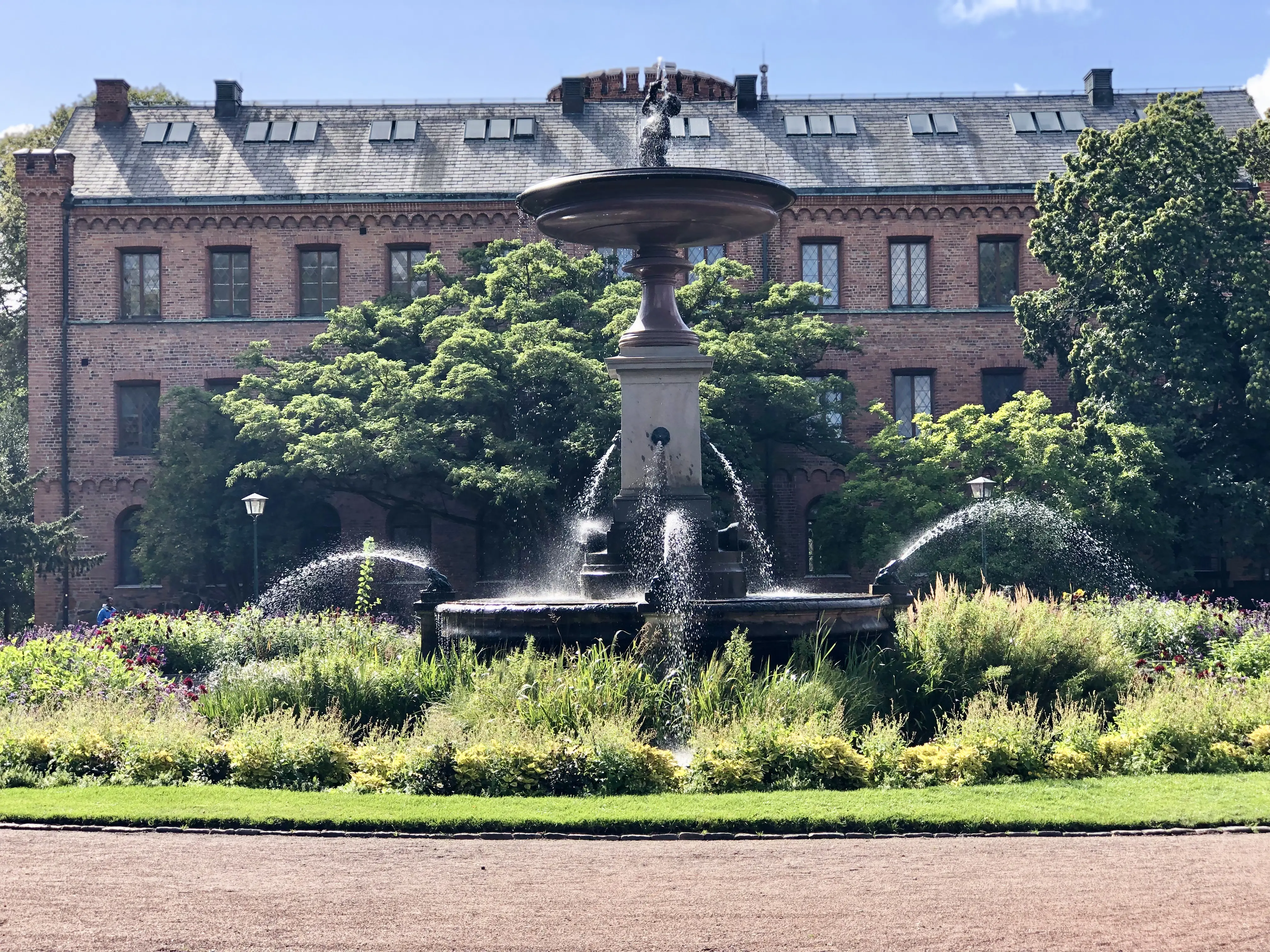 Fontänen i Lundagård omgiven av grönska. I bakgrunden Kungshuset.