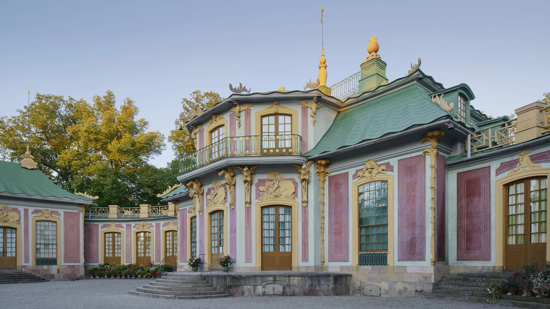 Kina slott, Drottningholm. Litet rödrosa slott med grönt, vågigt plåt-tak. Tak och fasad har skulpterad, gul dekor.