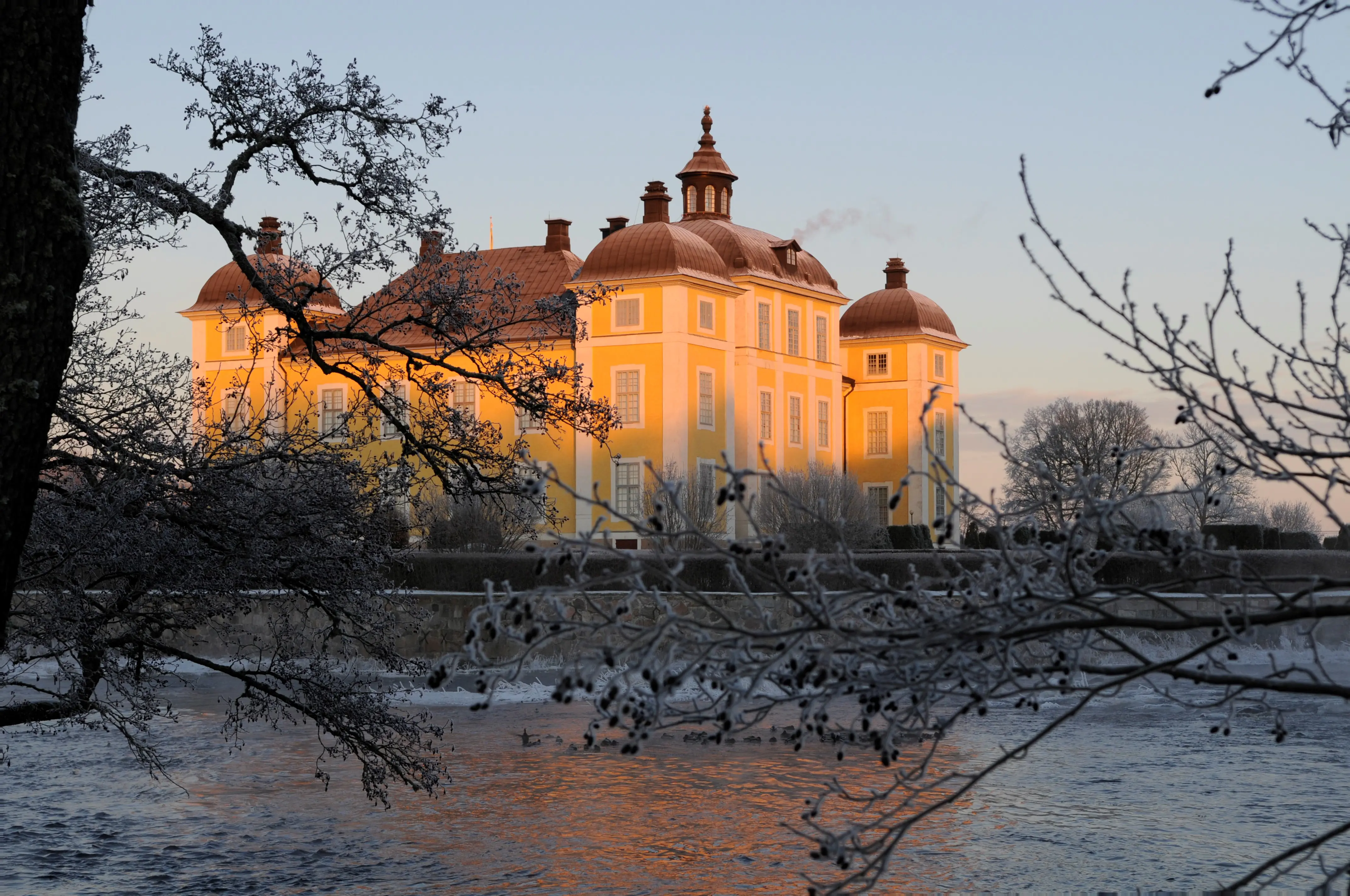 Strömsholms slott sett över Kolbäcksån. Solen lyser upp den gula fasaden. Vinter och frost.