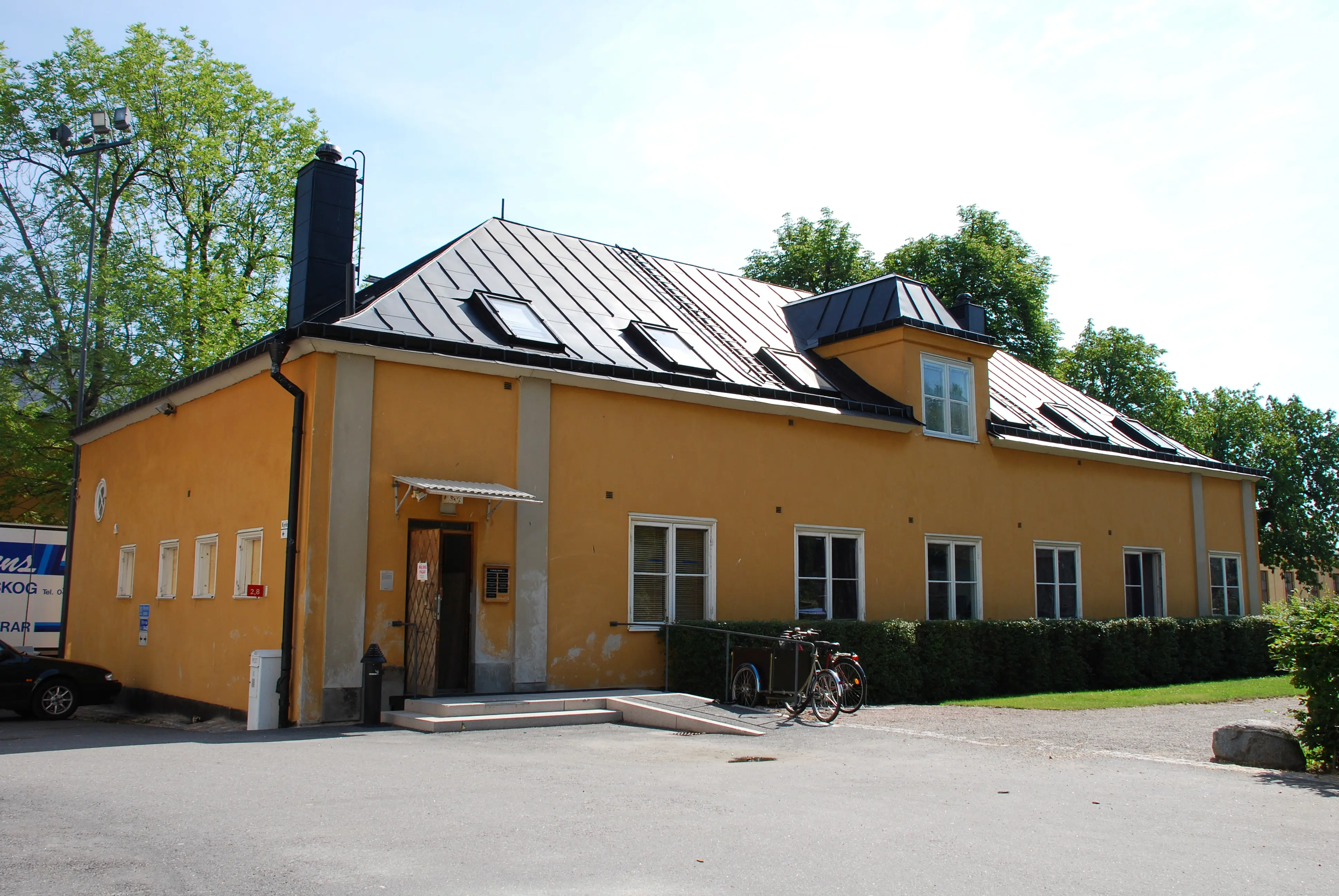 Marketenteriet på Skeppsholmen. Gulputsad byggnad med valmat svart plåt-tak. Taket har fönster och en tak-kupa.